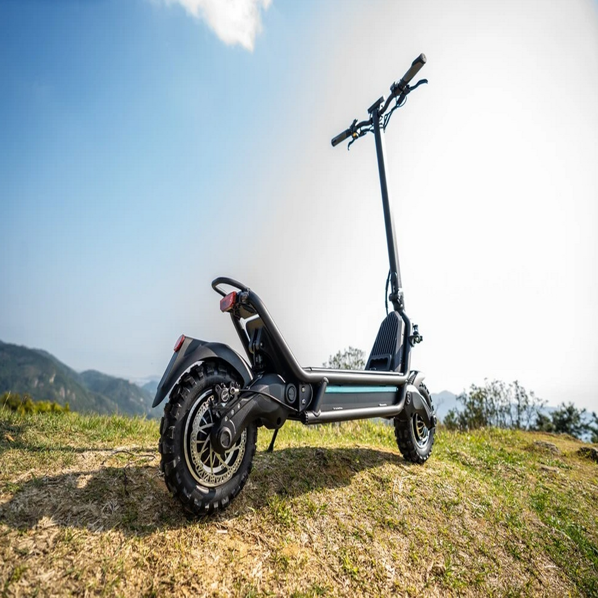 Uno scooter elettrico su una collina erbosa, con cielo blu e colline distanti.