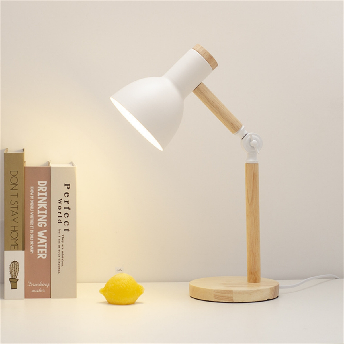 Eine weiße Schreibtischlampe mit Holzsockel und -hals beleuchtet Bücher und eine Zitrone.