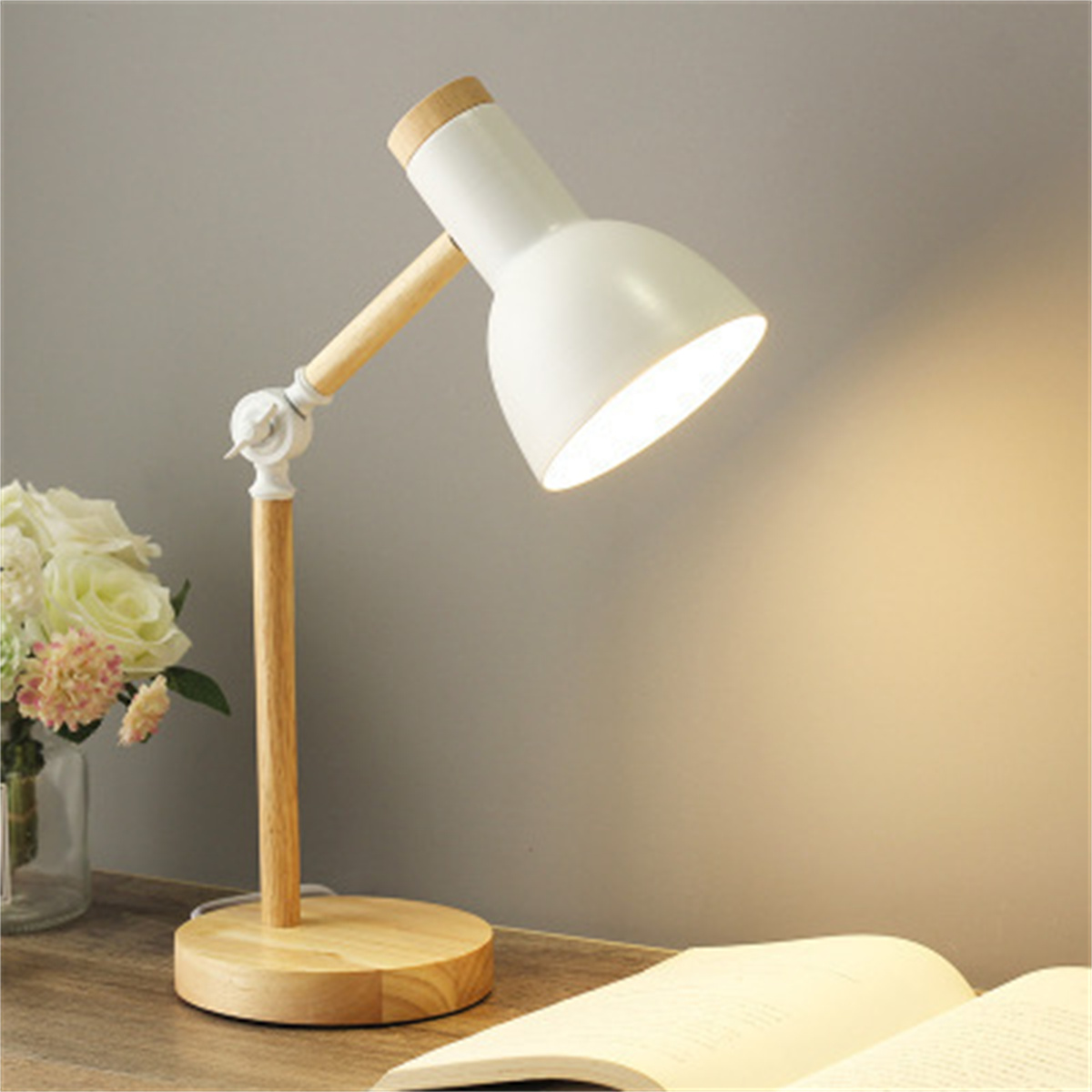 Weiße Schreibtischlampe mit Holzfuß und Arm. Sie ist eingeschaltet. Weiches Licht scheint.