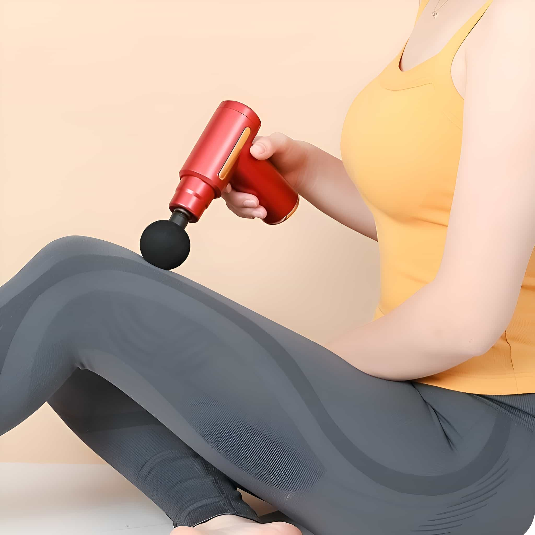 Frau mit roter Massagepistole, die ihr Bein massiert, während sie mit grauer Leggings sitzt.