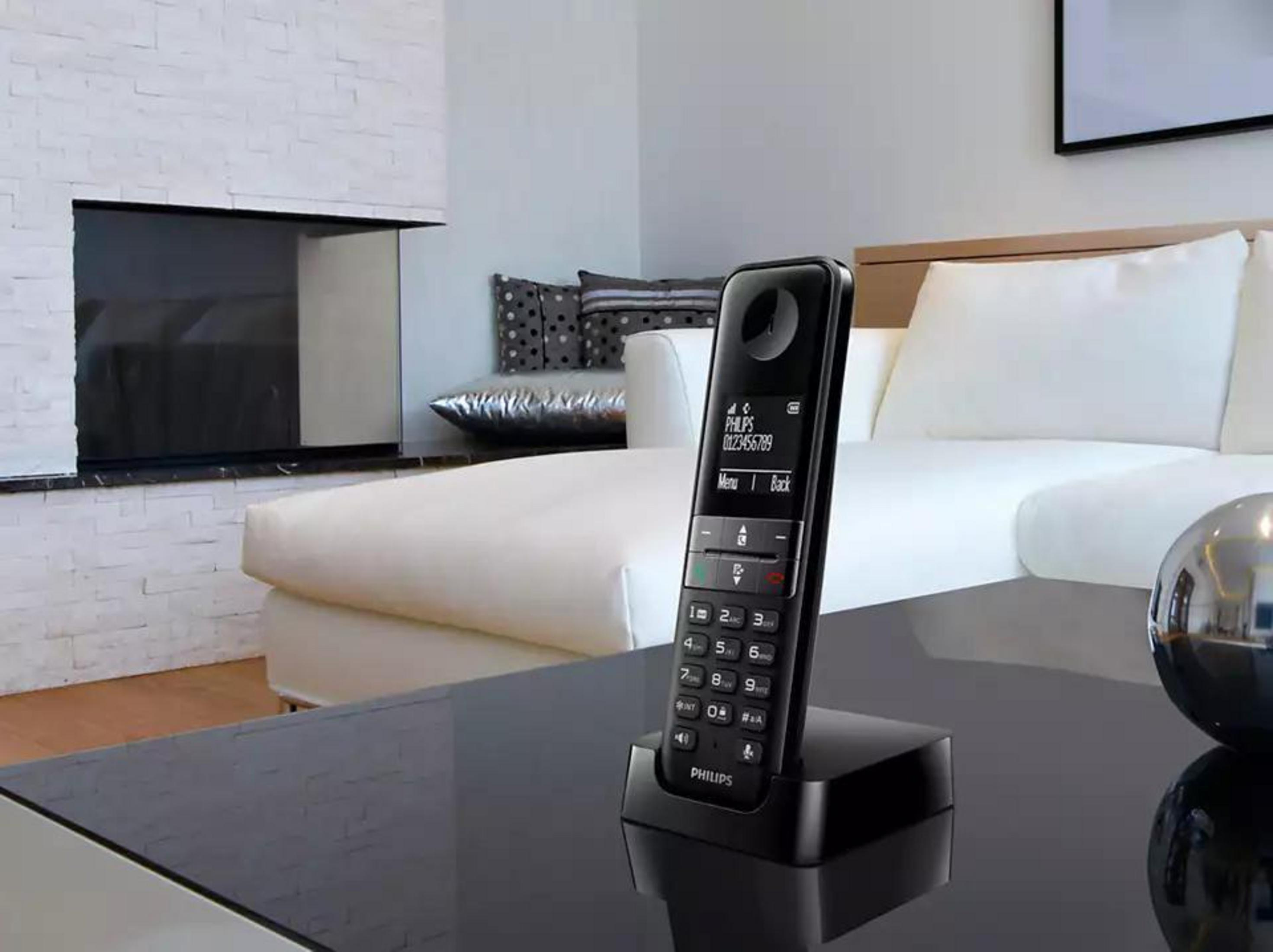 Un téléphone sans fil noir sur son socle, posé sur une table noire dans un salon.