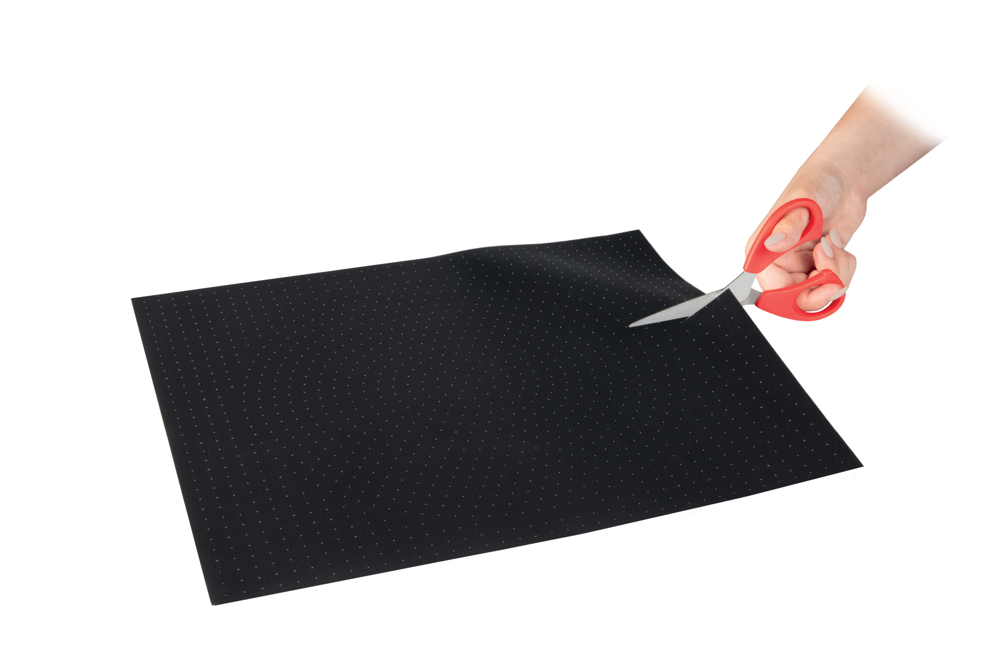 Die Hand einer Person schneidet mit einer roten Schere ein schwarzes Blatt Papier mit weißen Punkten auf weißem Hintergrund.