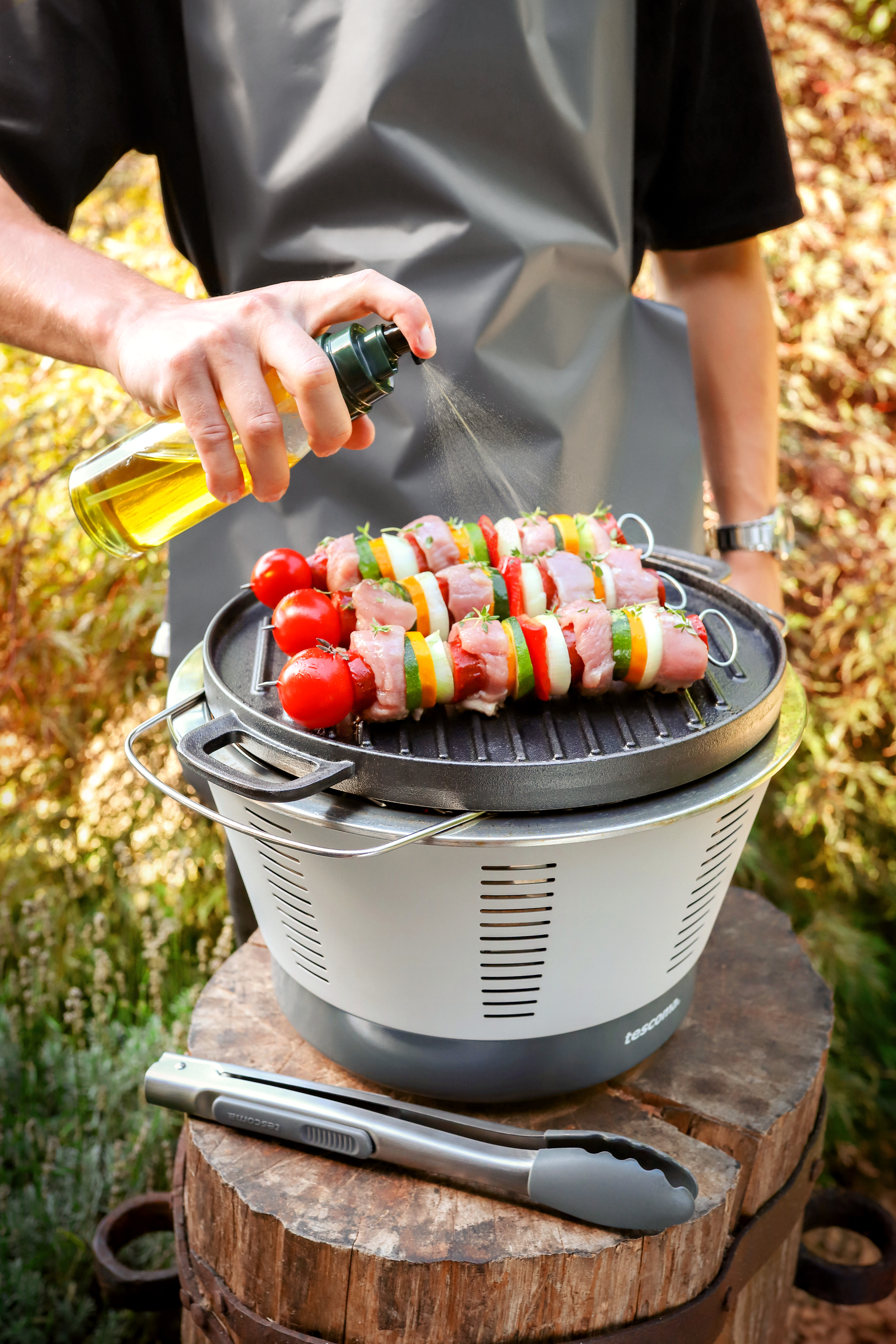 Mann, der Spieße auf einem kleinen Grill grillt. Er sprüht Öl auf das Essen.