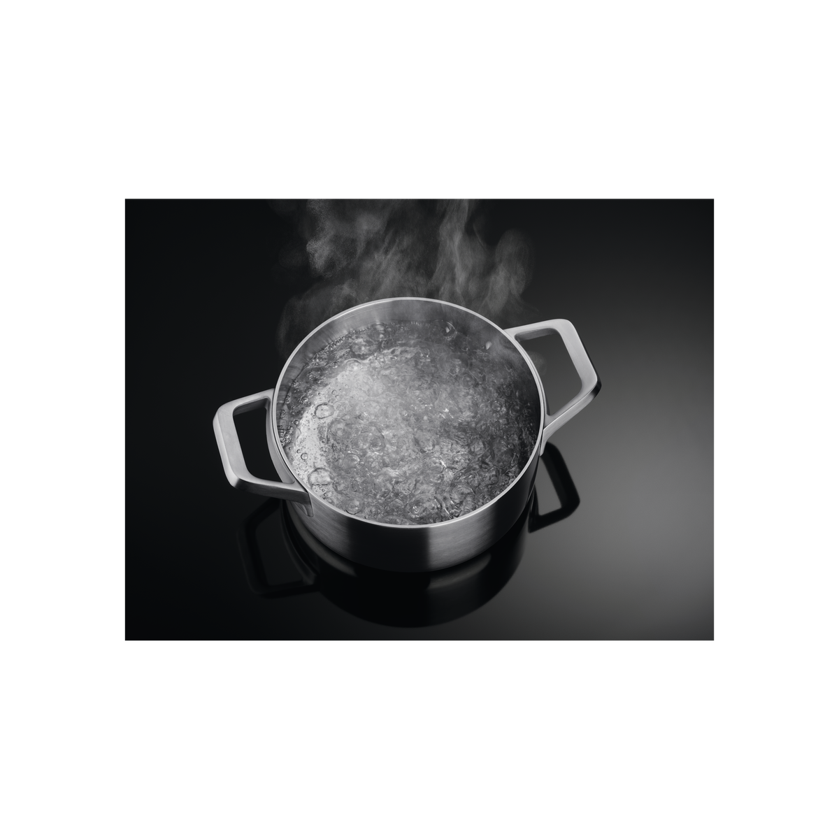 Olla de acero inoxidable con agua hirviendo en una estufa negra, vapor subiendo.