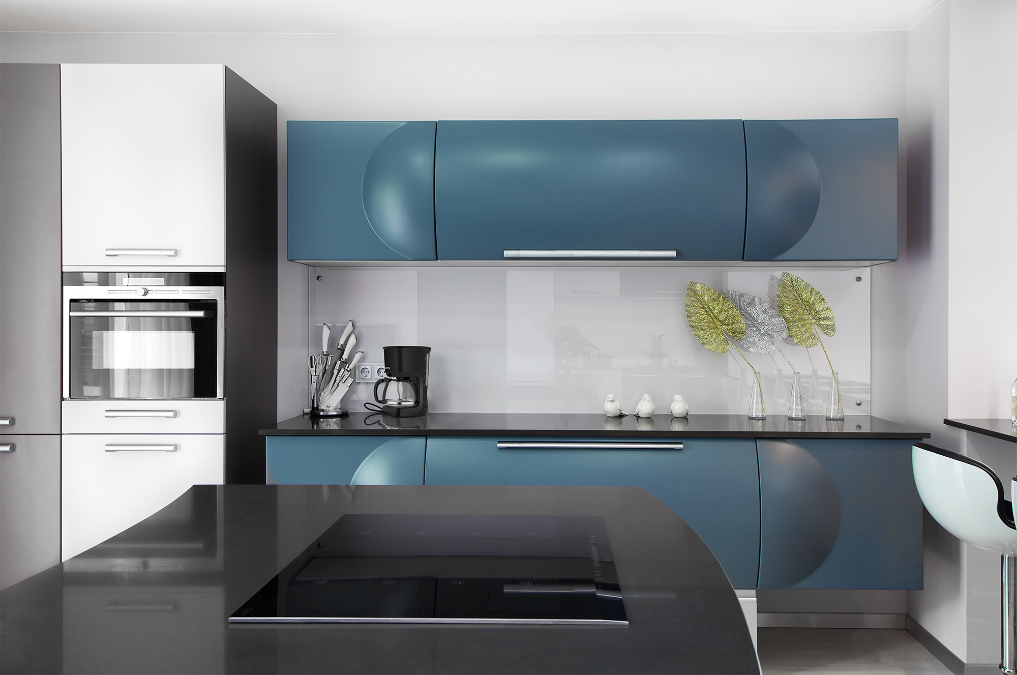 Nowoczesna kuchnia z niebieskimi szafkami, czarnymi blatami i wbudowanymi urządzeniami.