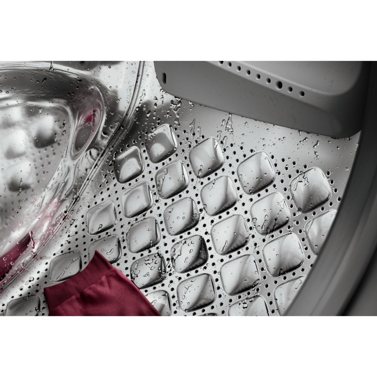 Wewnątrz bębna pralki z czerwonym elementem odzieży. Powierzchnia metaliczna i błyszcząca.