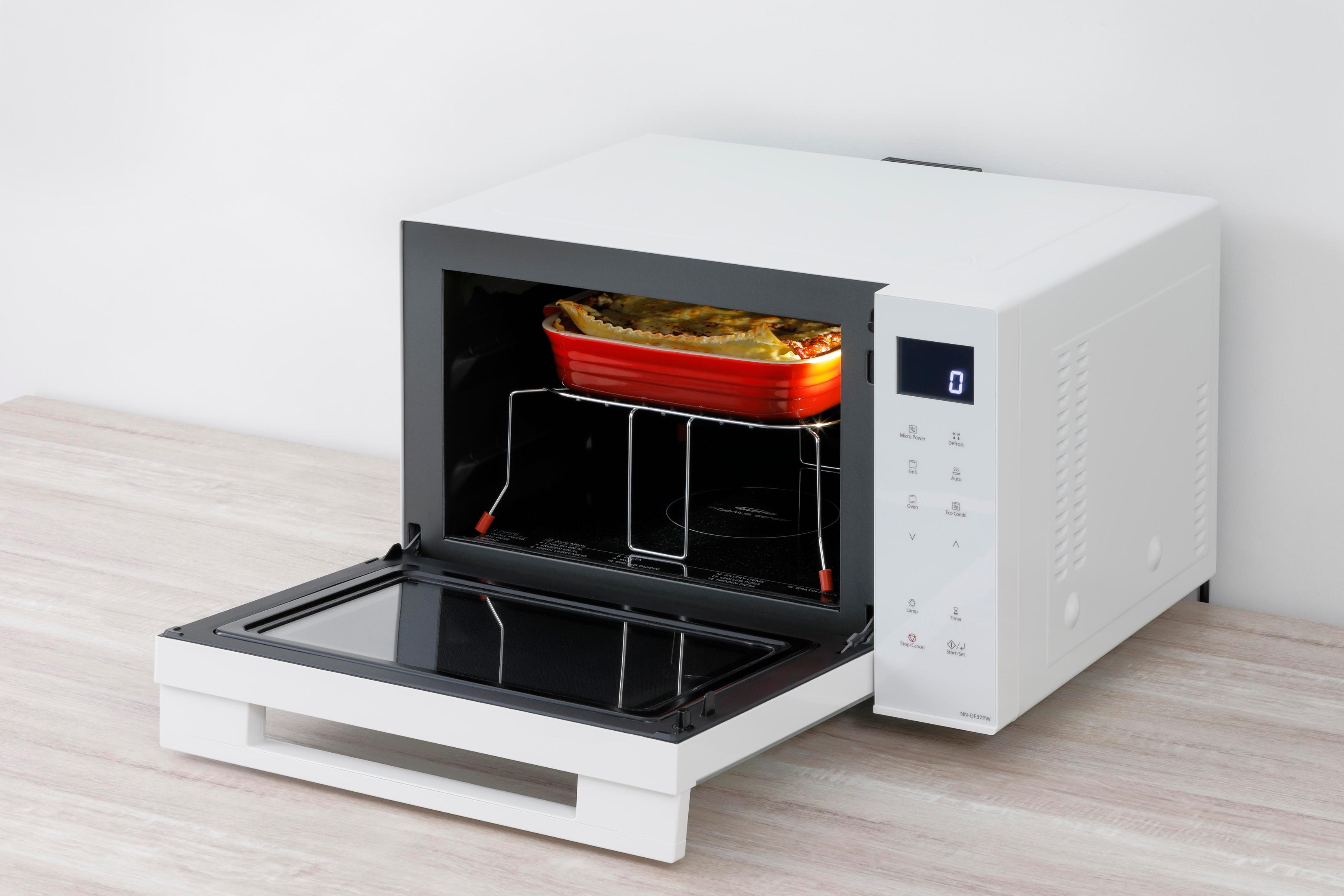 Biała kuchenka mikrofalowa z czerwoną potrawą w środku. Drzwi są otwarte. Tło to jasna ściana.