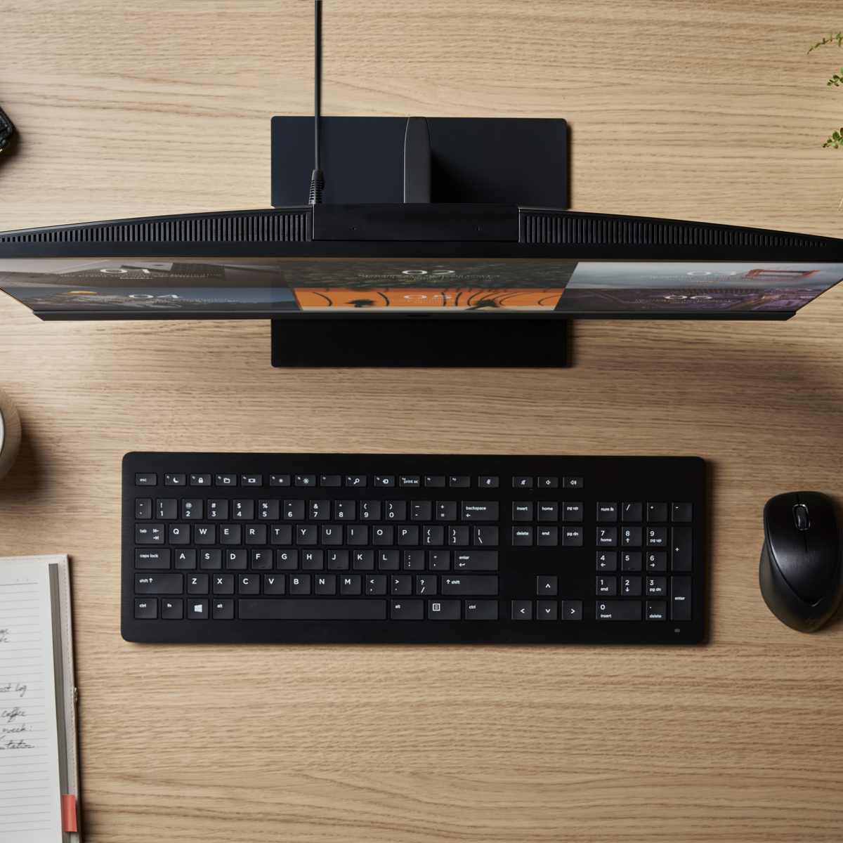 Czarna klawiatura, mysz i monitor na drewnianym biurku. Monitor wyświetla obrazy.