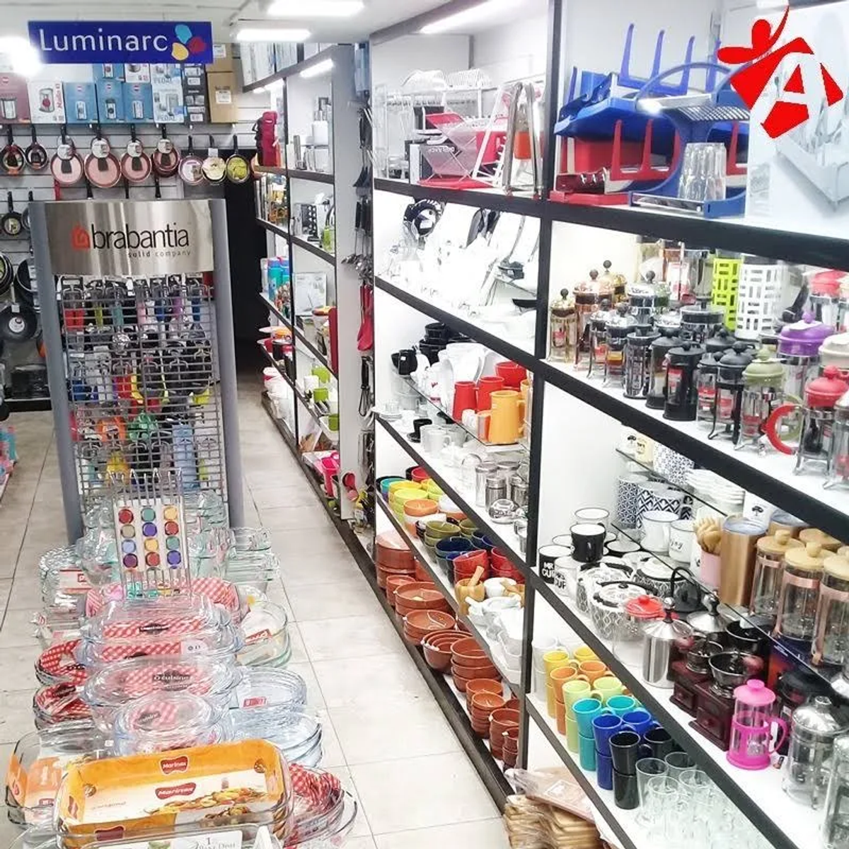 Dobrze zaopatrzony wystrój sklepu z półkami wypełnionymi naczyniami kuchennymi i artykułami gospodarstwa domowego. Białe ściany.