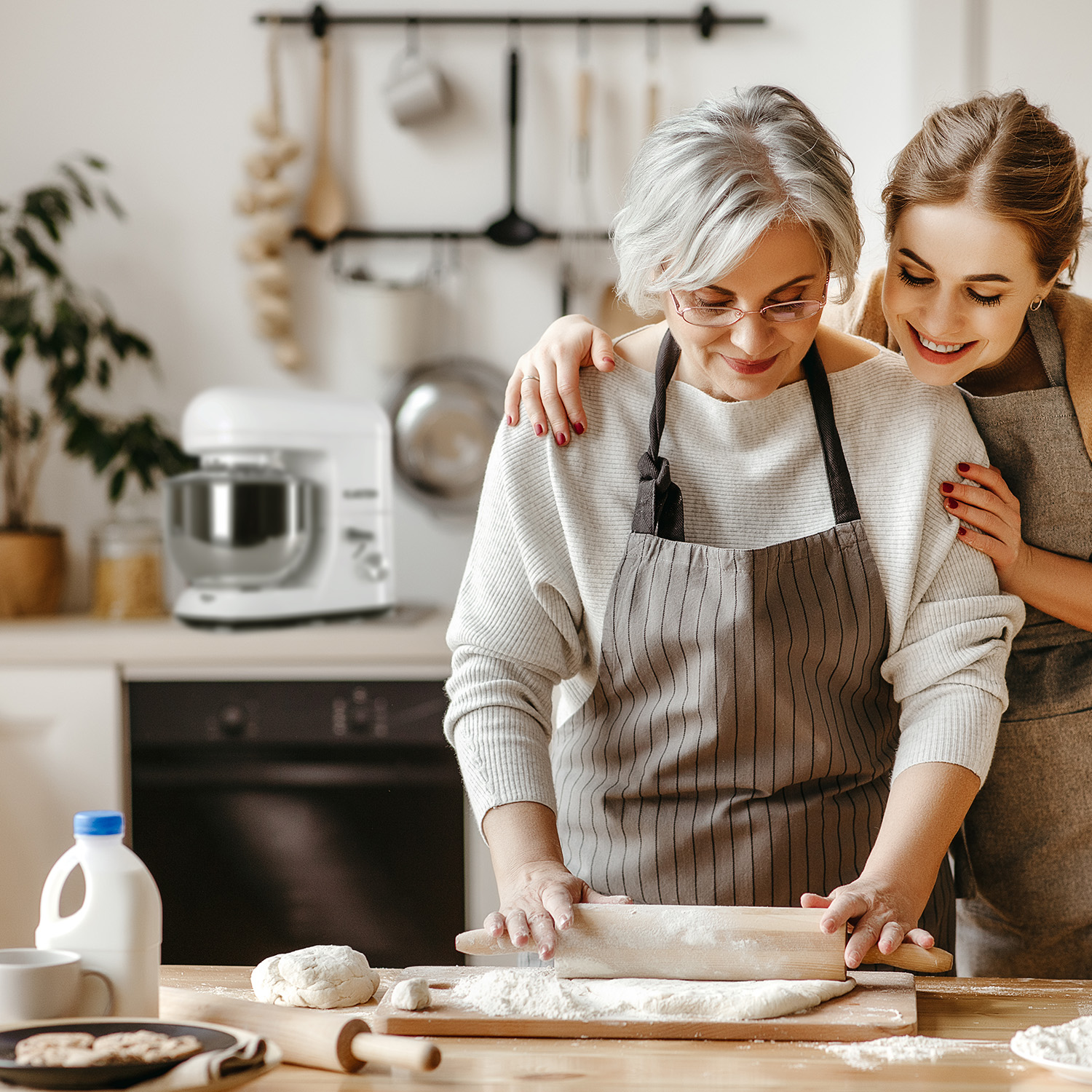 Zwei Frauen backen zusammen in einer Küche. Eine rollt Teig aus.