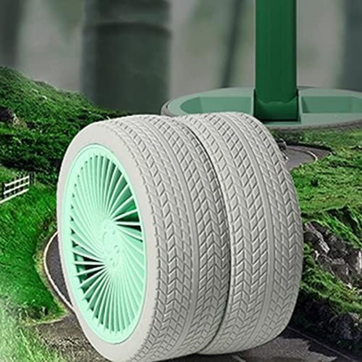 Dos neumáticos con una rueda verde, colocados frente a un paisaje verde con una carretera.