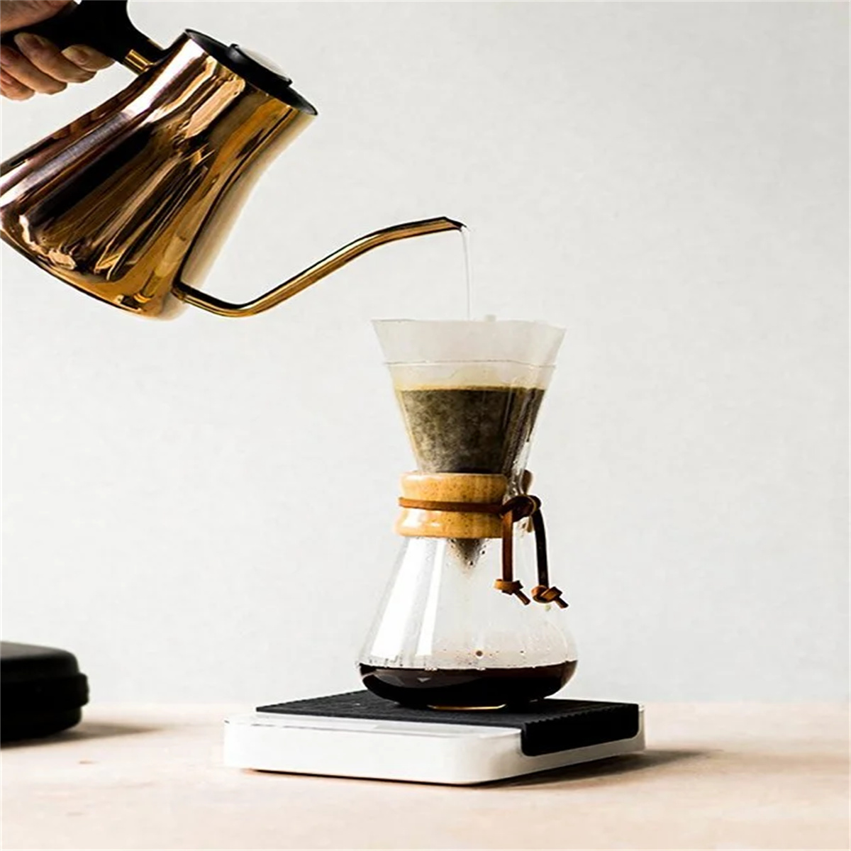 Kaffeezubereitung: Ein goldener Wasserkocher gießt Wasser in eine Glas-Chemex mit Kaffeepulver.