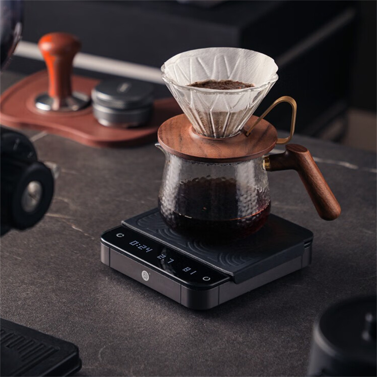 Kaffeezubereitung mit Pour-Over-Methode, zeigt dunklen Kaffee in einer Karaffe auf einer Waage, mit Holzakzenten.