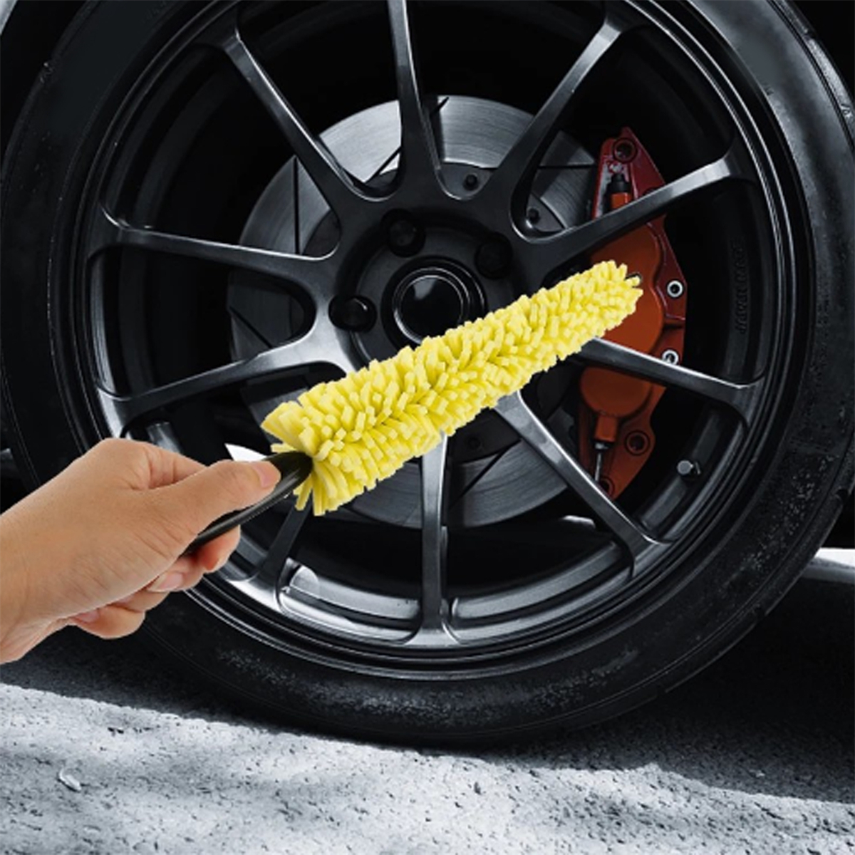 Eine Hand, die eine gelbe Autoreinigungbürste hält, mit dem Rad im Hintergrund.