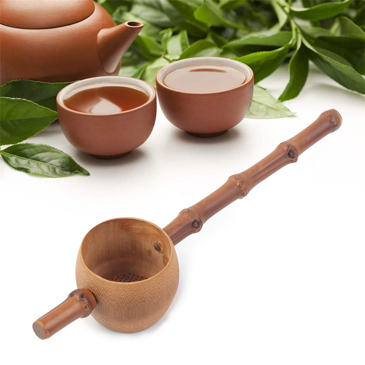 Teeset mit Teekanne, zwei Tassen und einem Bambus-Teesieb auf weißer Oberfläche.
