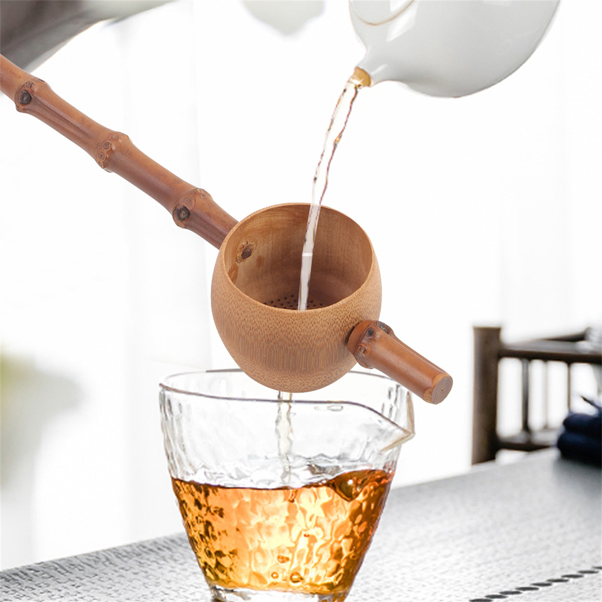 Tee wird aus einer weißen Teekanne in einen Bambus-Teelöffel und dann in ein Glas gegossen.