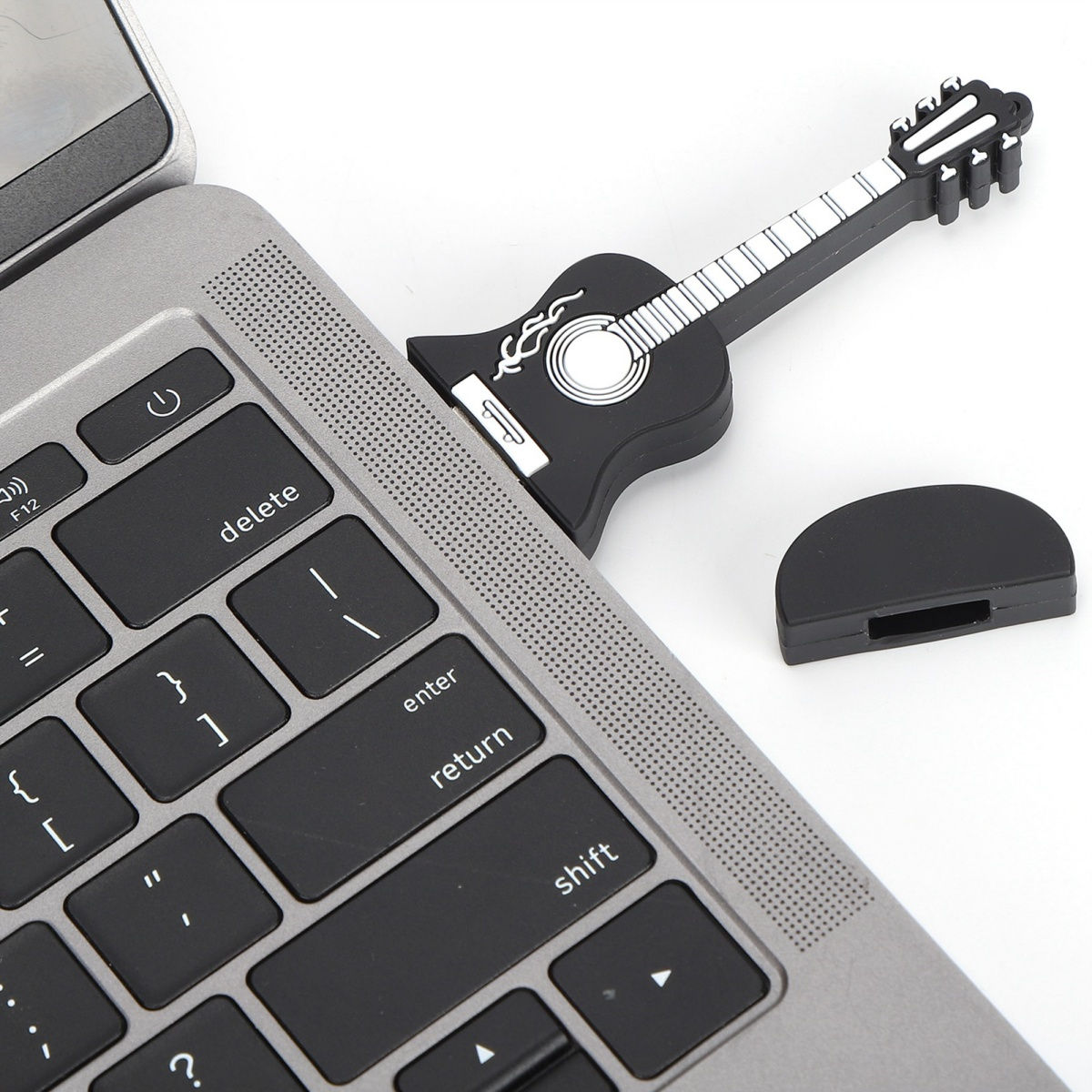 Schwarzer USB-Stick in Gitarrenform in einem Laptop, daneben eine schwarze Kappe.