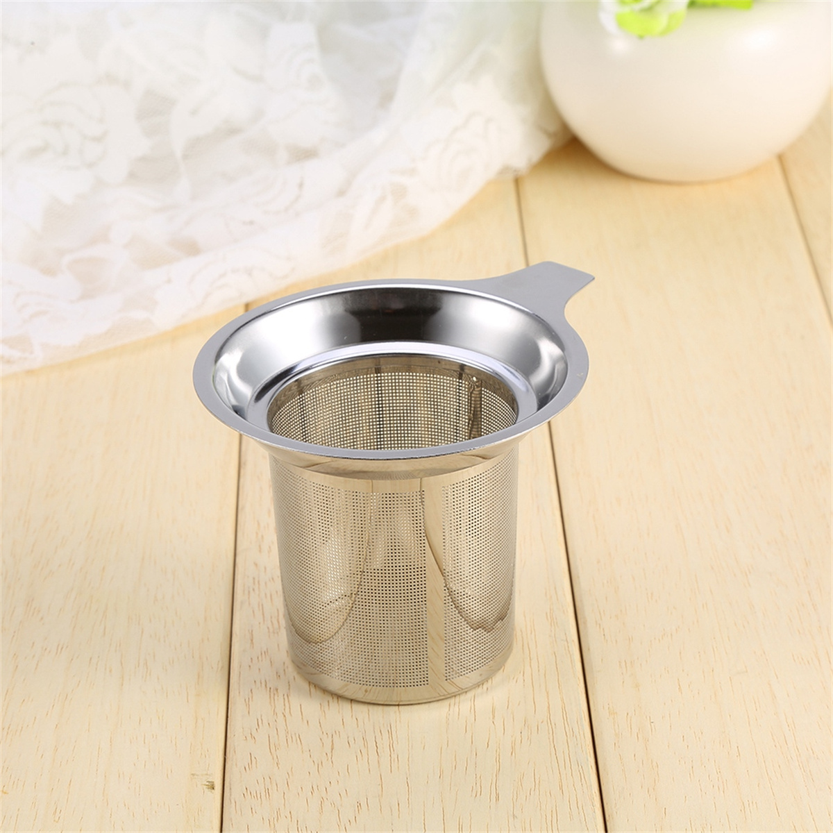 Eine silberne Tee-Infuser-Tasse auf einer Holzoberfläche, mit einem Griff.