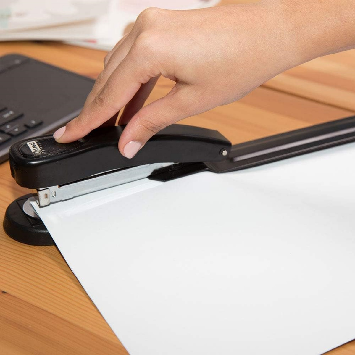 Eine Hand, die einen schwarzen Tacker verwendet, um ein weißes Blatt Papier zu tackern.