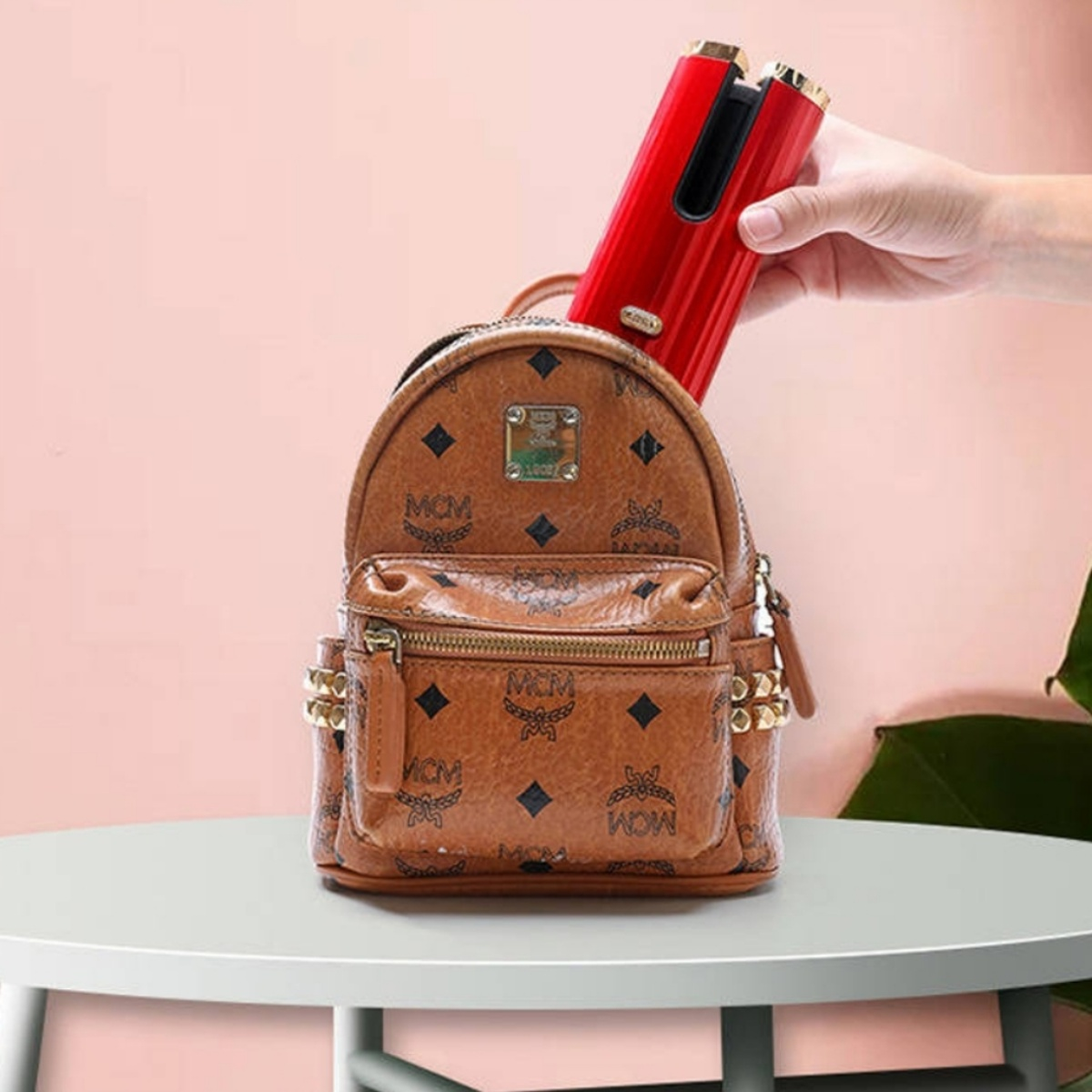 Ein roter Lockenstab befindet sich in einem braunen MCM-Rucksack auf einem weißen Tisch.