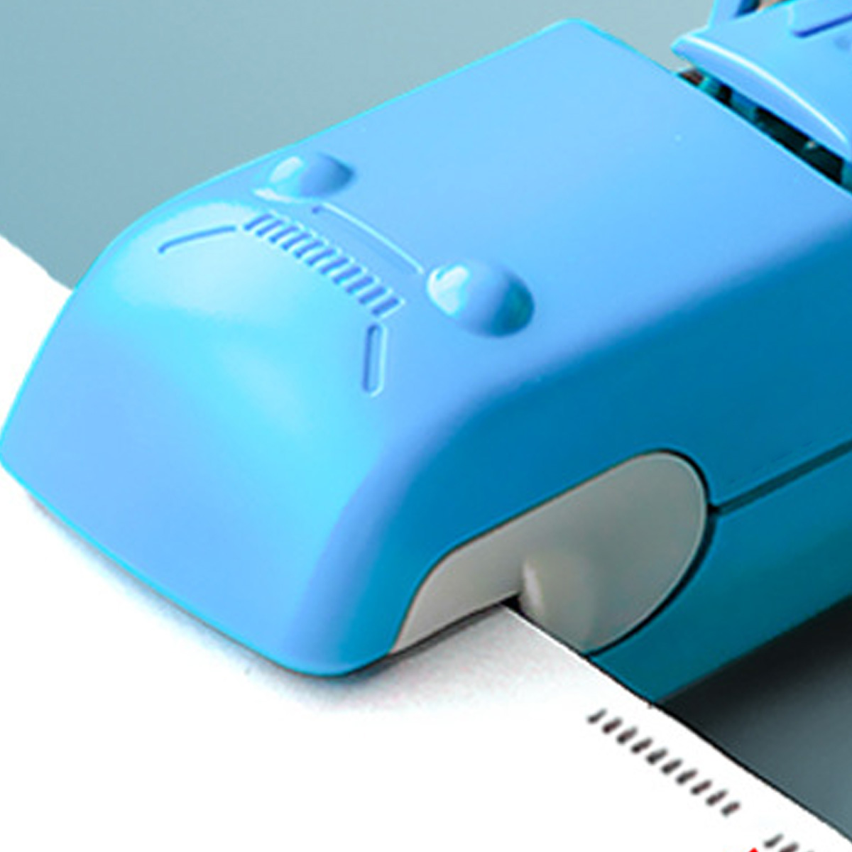 Nahaufnahme eines blauen Hefters, der ein weißes Papier heftet. Der Hefter hat ein lächelndes Gesicht.