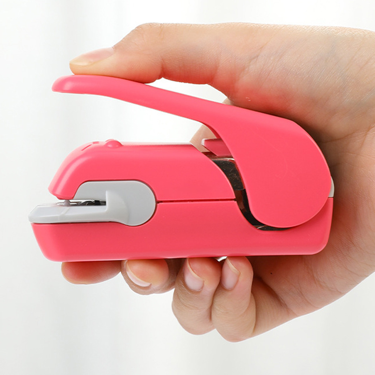 Ein rosa Tacker wird von einer Hand gehalten. Der Tacker ist klein und hat eine abgerundete Oberseite.