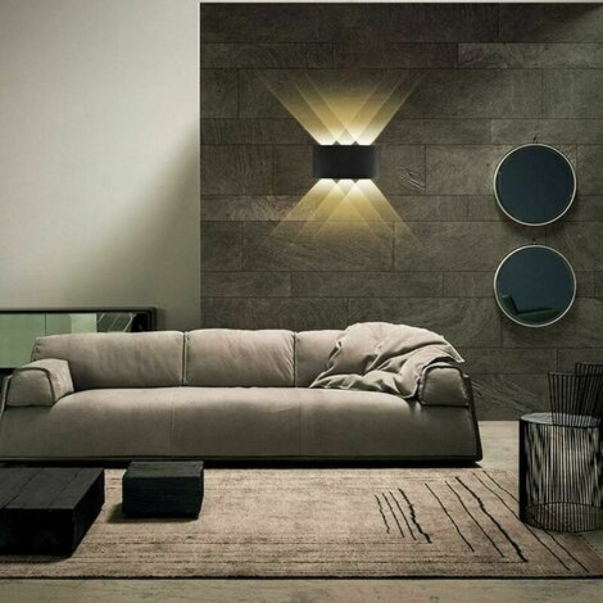 Ein modernes Wohnzimmer mit grauem Sofa, schwarzer Wand mit Leuchte und zwei runden Spiegeln.