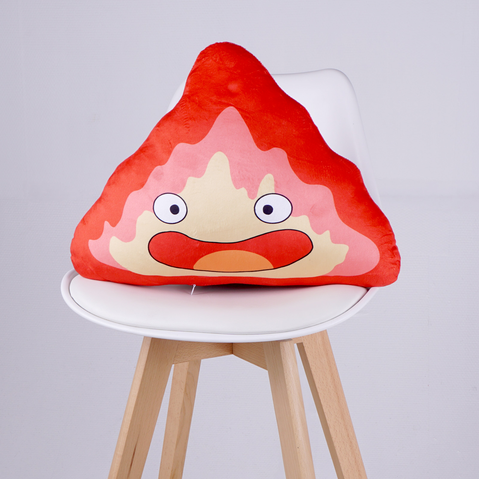 Ein rotes, dreieckiges Plüschtier mit Gesicht, das auf einem weißen Stuhl sitzt.