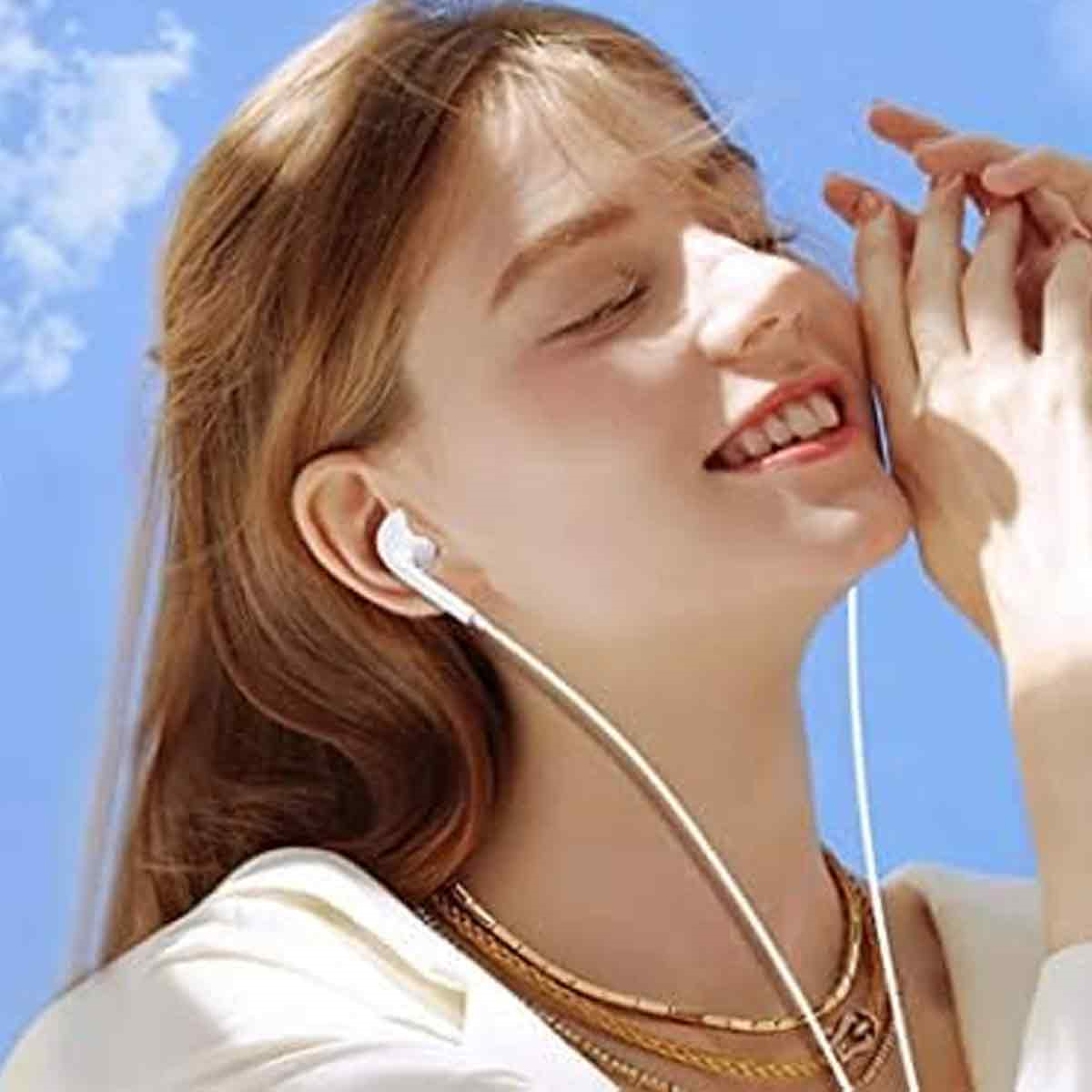Frau mit Ohrhörern lächelt vor blauem Himmel.