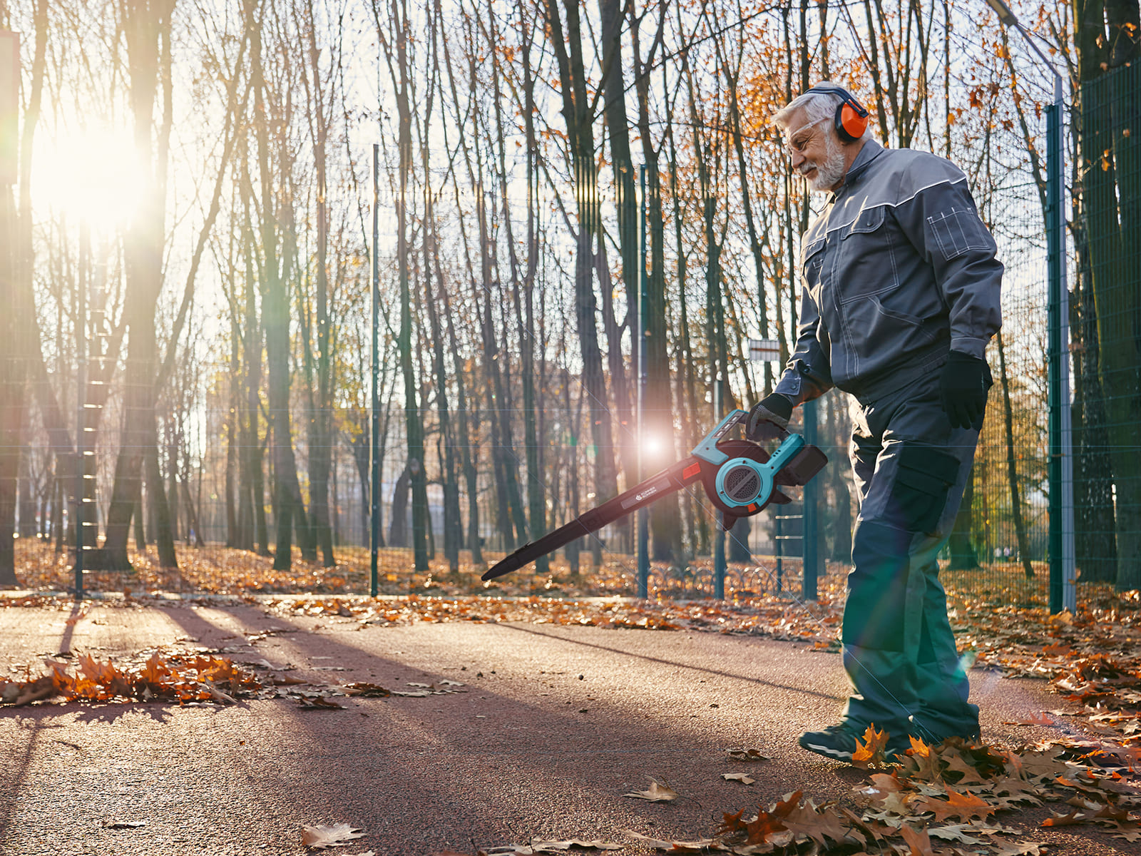 Een oudere man met een bladblazer in de herfst, bladeren van een pad aan het verwijderen.