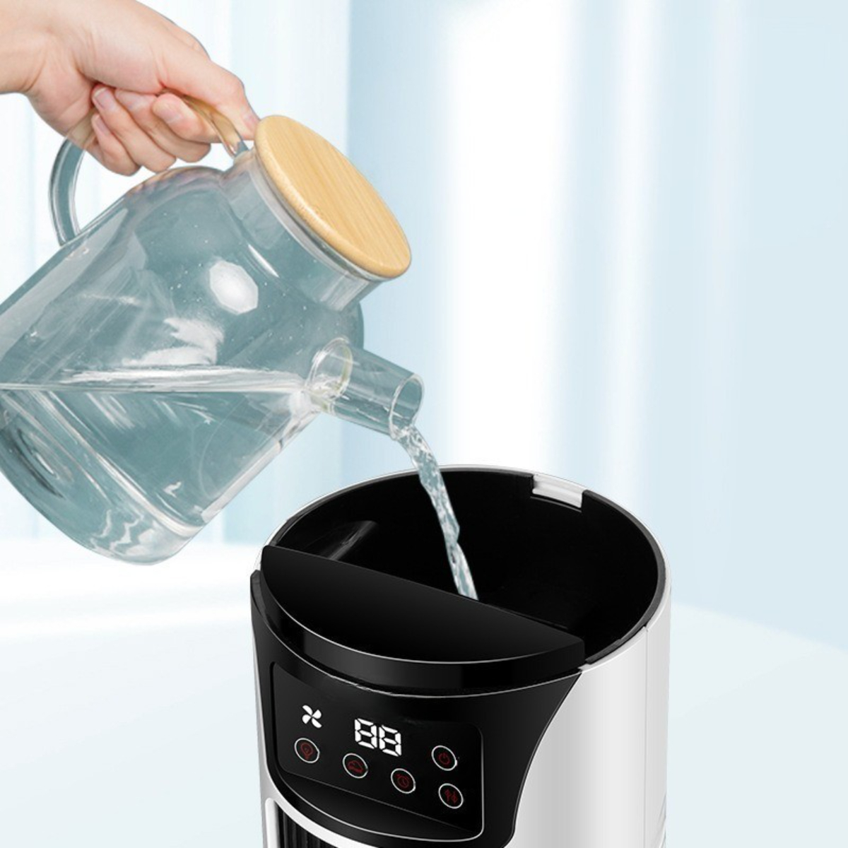 Eine Hand, die Wasser aus einer Glaskaraffe in einen schwarz-weißen Luftkühler gießt.