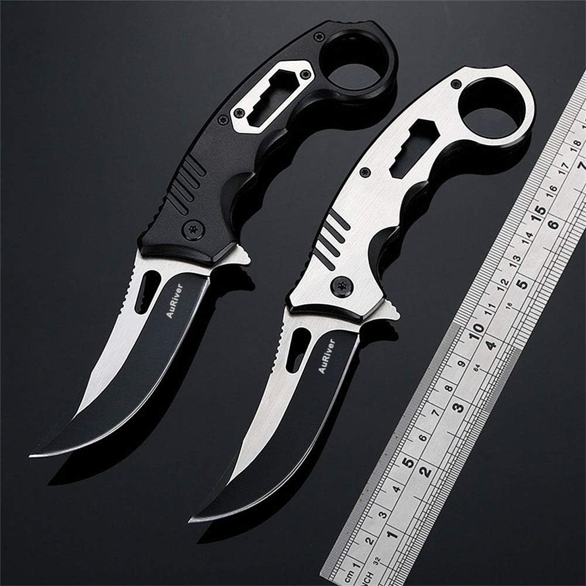 Zwei schwarze und silberne Messer mit gebogenen Klingen liegen auf einer glänzenden Oberfläche neben einem Lineal.
