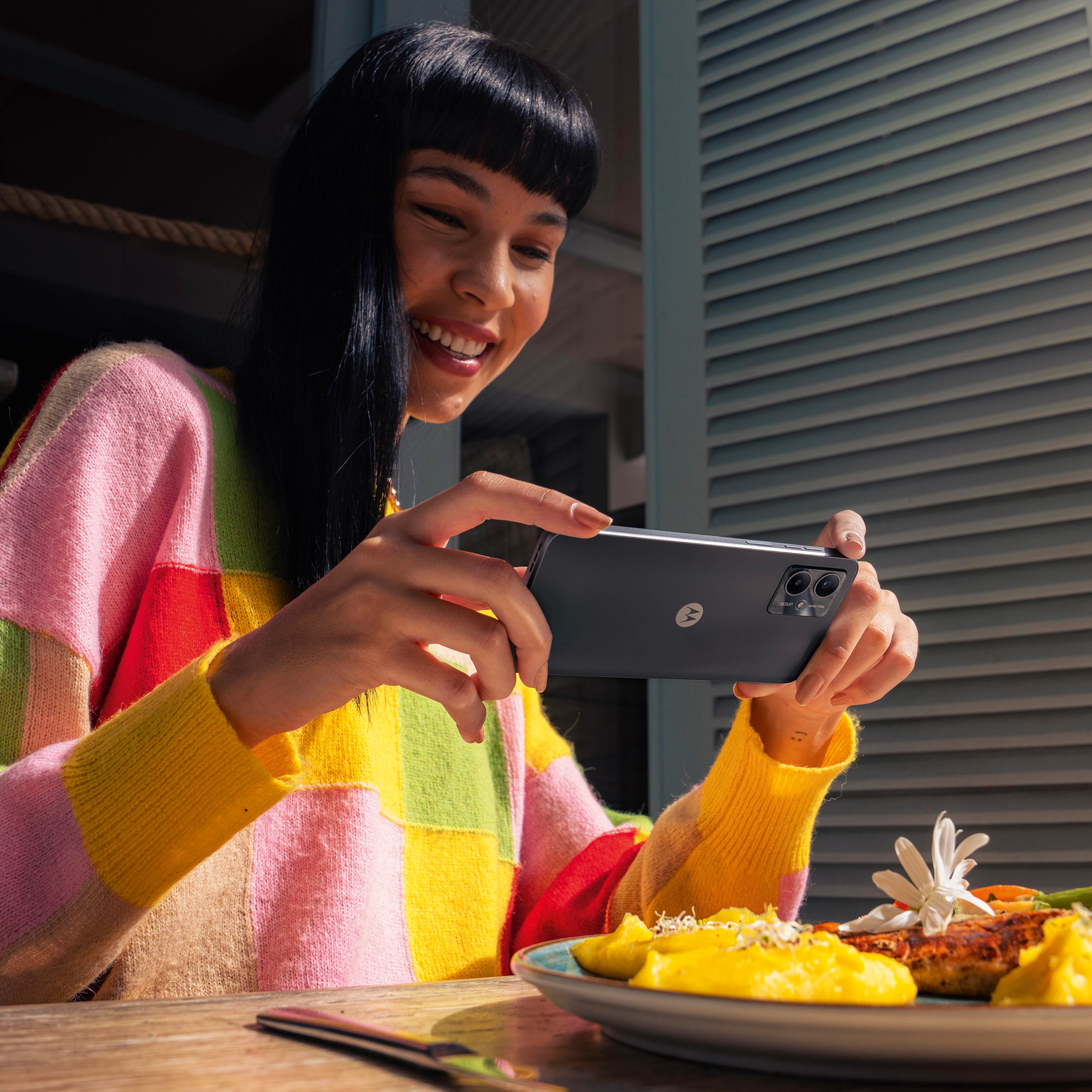 Una mujer sosteniendo un teléfono tomando una foto de comida en una mesa afuera.
