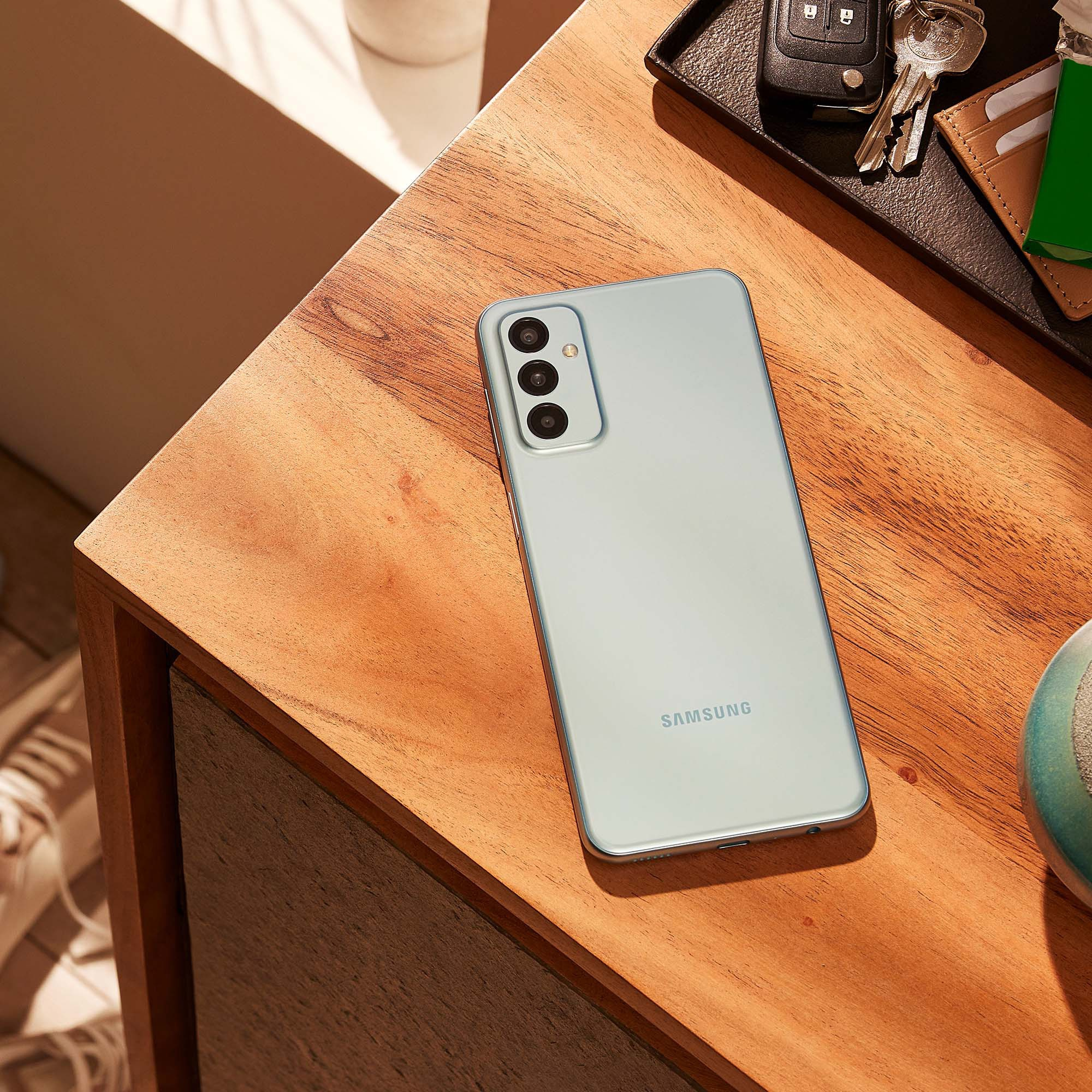 Smartphone auf einem Holztisch mit Schlüsseln, einer Geldbörse und einem grünen Gegenstand.