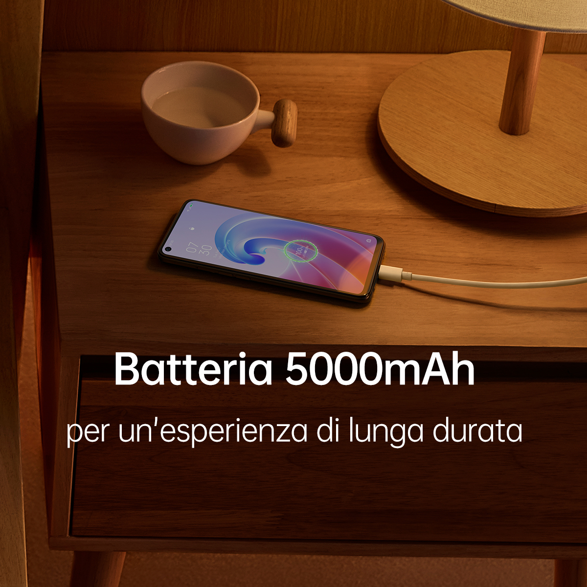 Un téléphone en charge sur une table de nuit avec une lampe et une tasse.