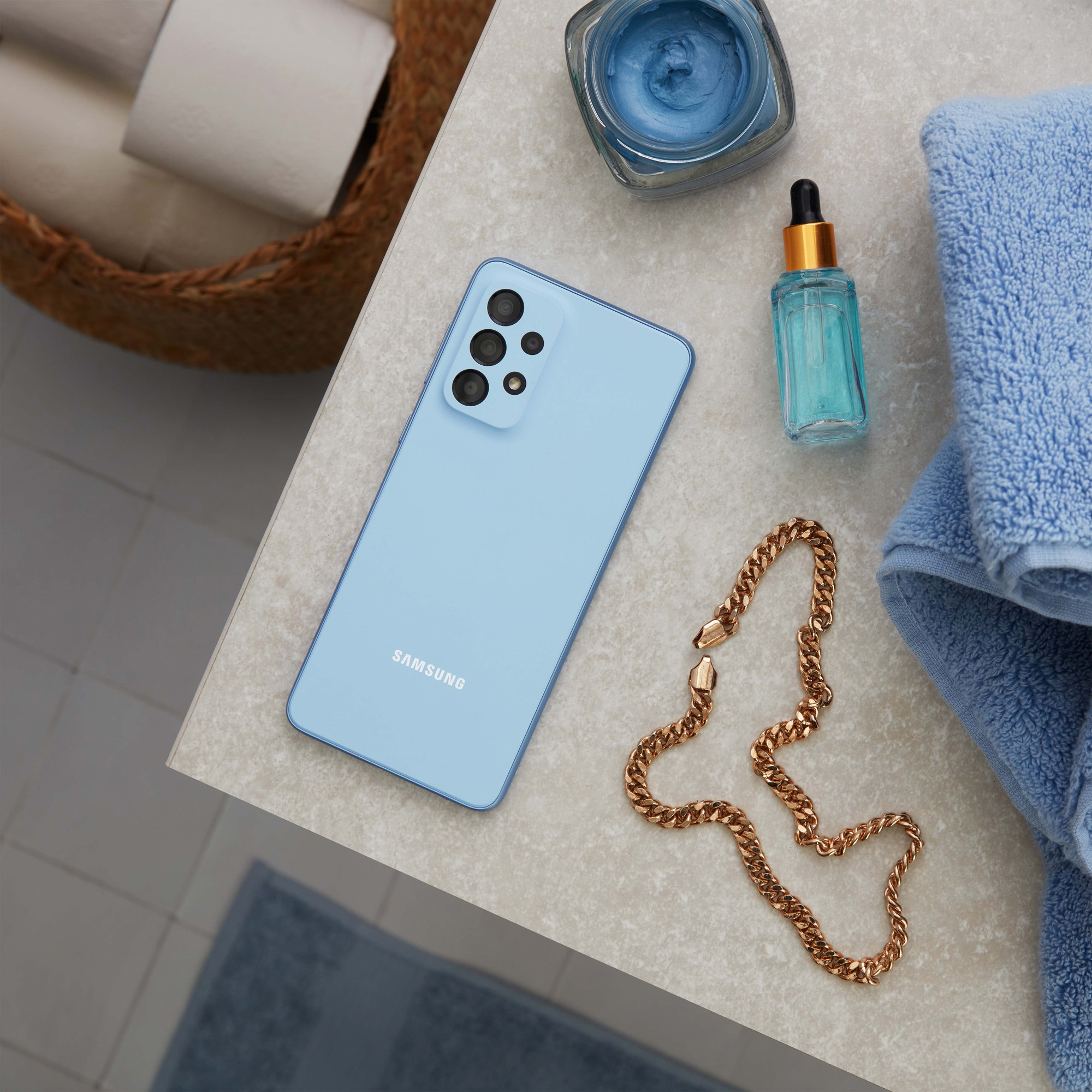 Smartfon, produkty do pielęgnacji skóry i biżuteria na powierzchni z ręcznikami i wiklinowym koszem.