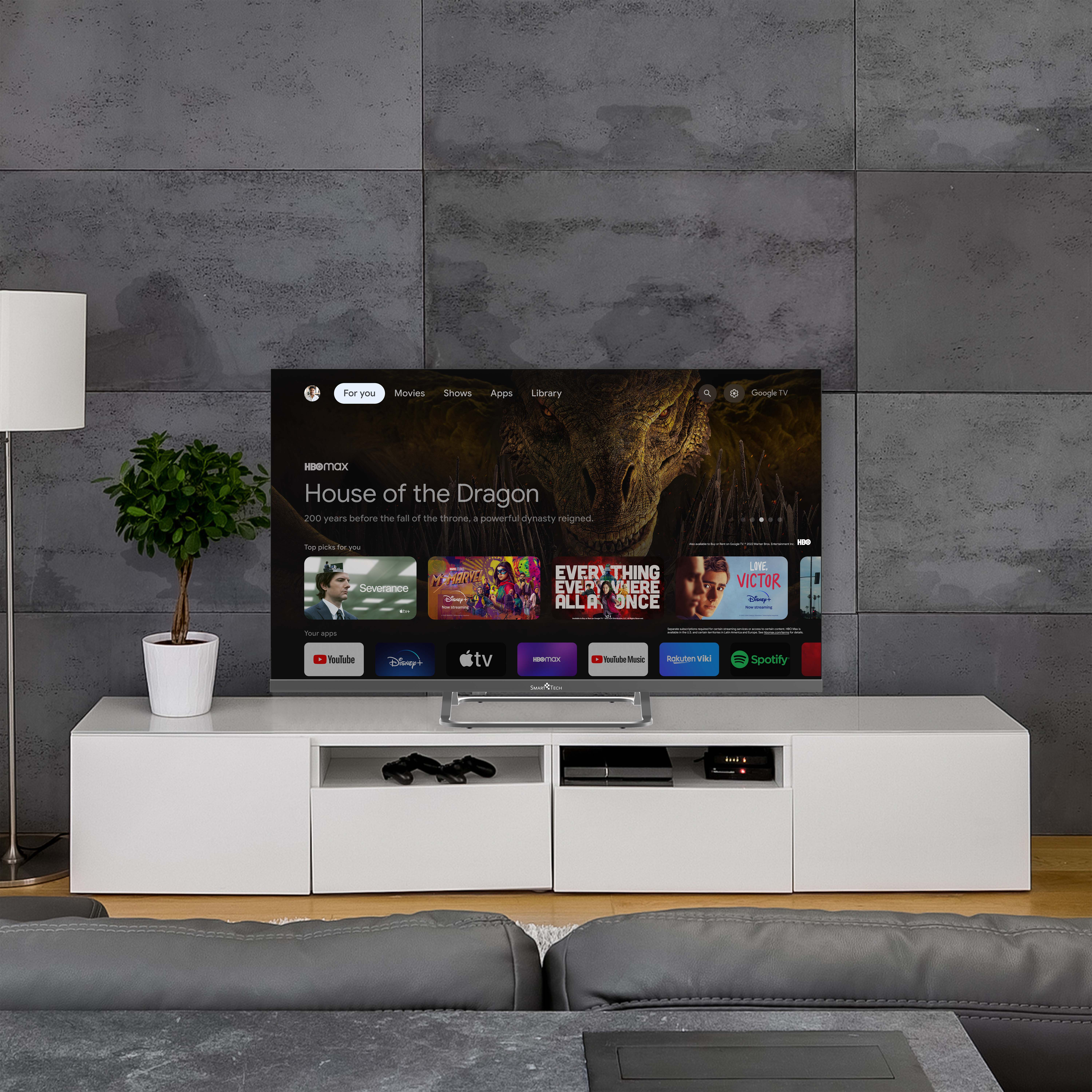 Biała szafka RTV z telewizorem wyświetlającym interfejs usługi streamingowej, z rośliną i lampą.