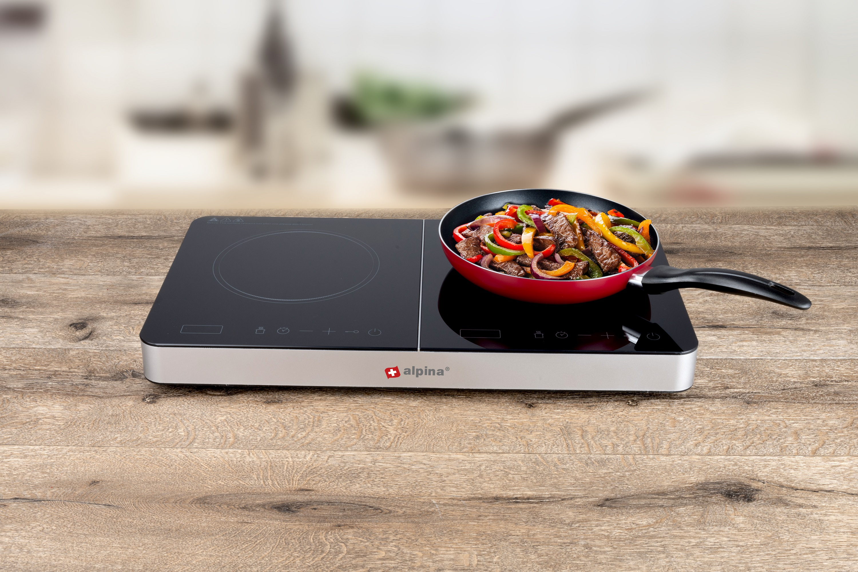 An induction cooktop with a pan of stir-fry food sits on a wooden surface.