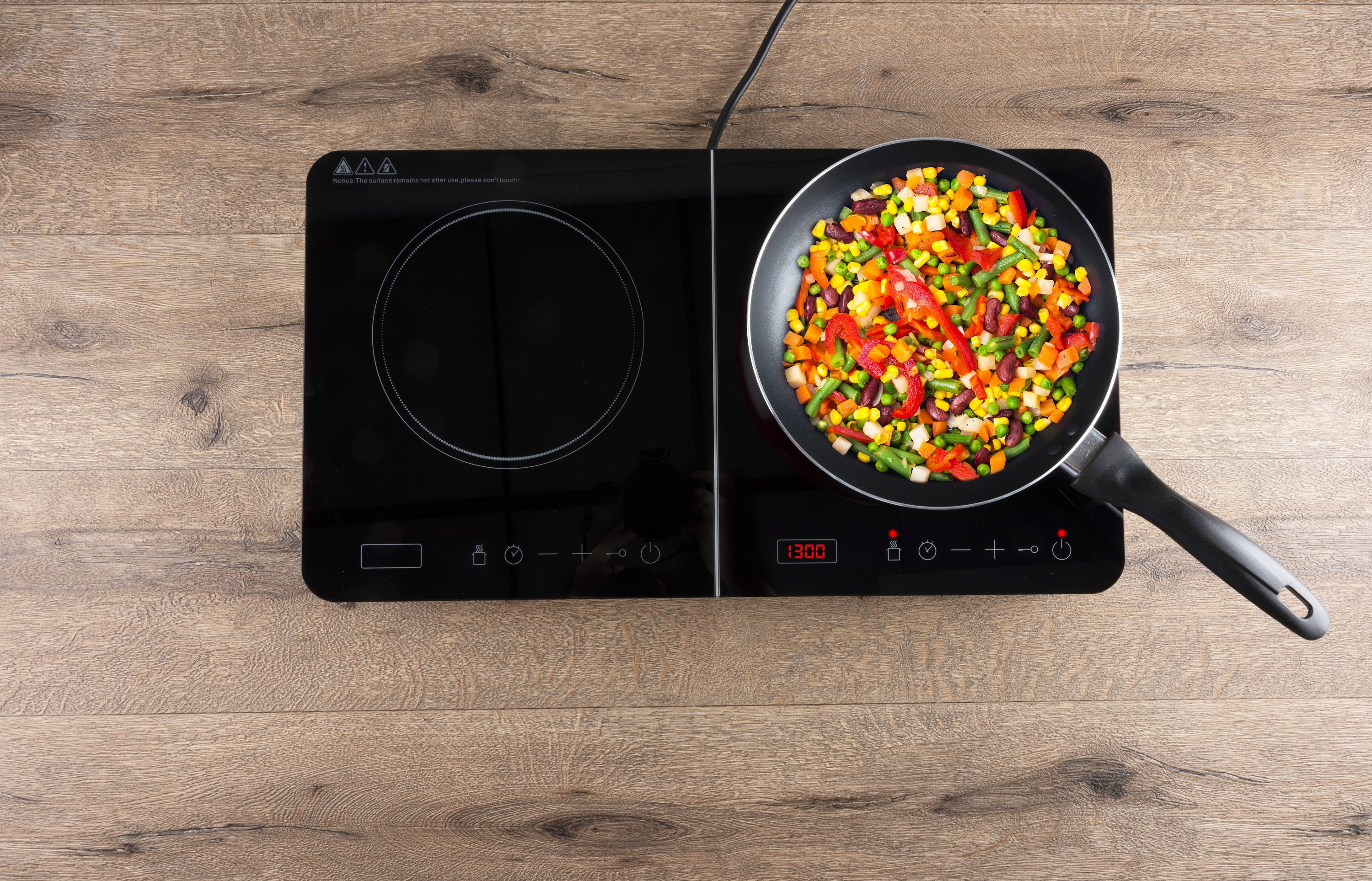 An induction stove with a pan of cooked vegetables sitting on it.