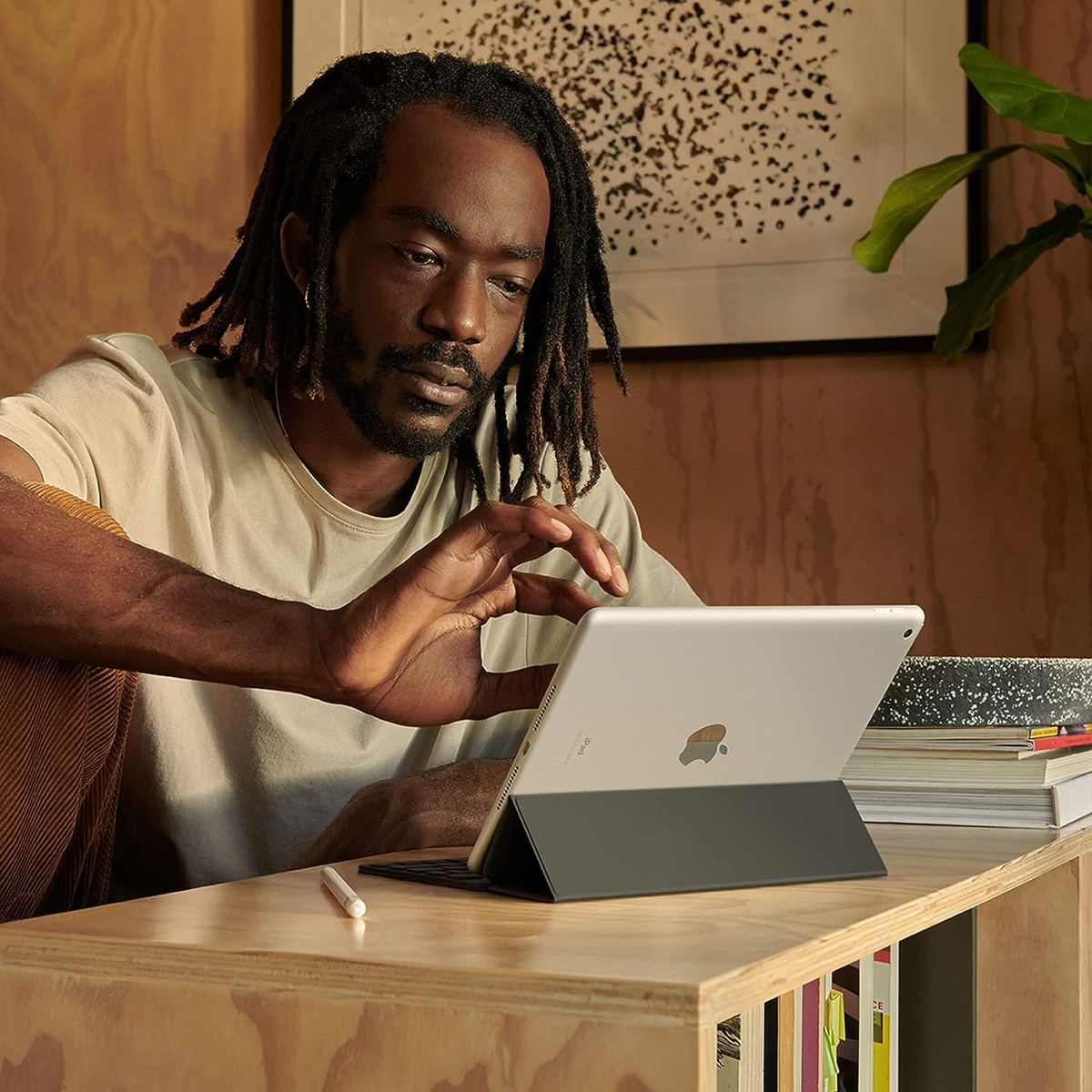 Mężczyzna używający iPada z klawiaturą na drewnianym biurku, z książkami i rośliną.