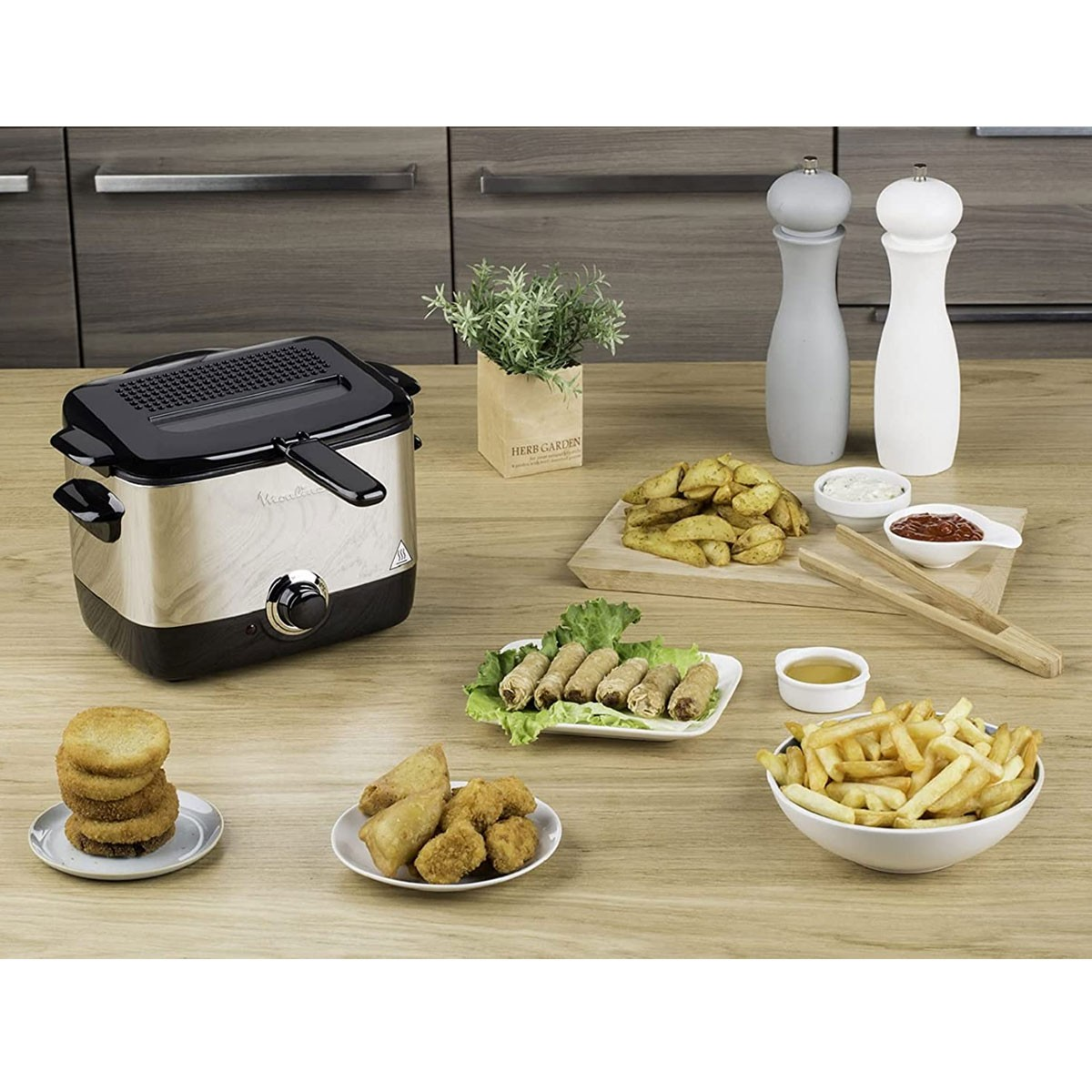 Frytkownica z różnymi potrawami, takimi jak frytki, nuggetsy, sajgonki i sosy na stole.