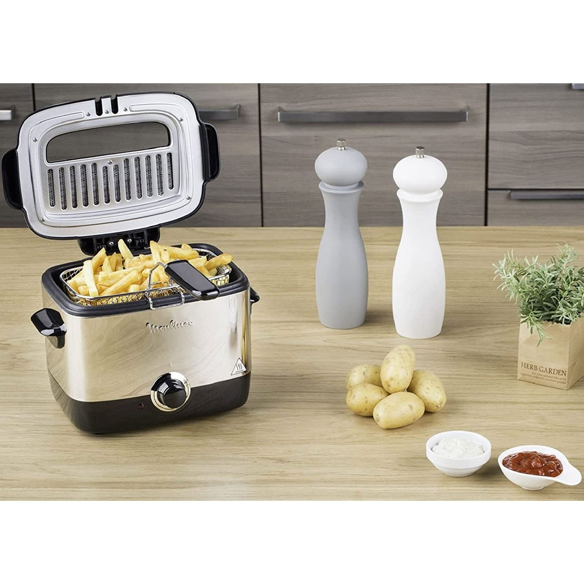Otwarta frytownica z frytkami, solniczkami i pieprzniczkami, ziemniakami i małą miseczką sosu.