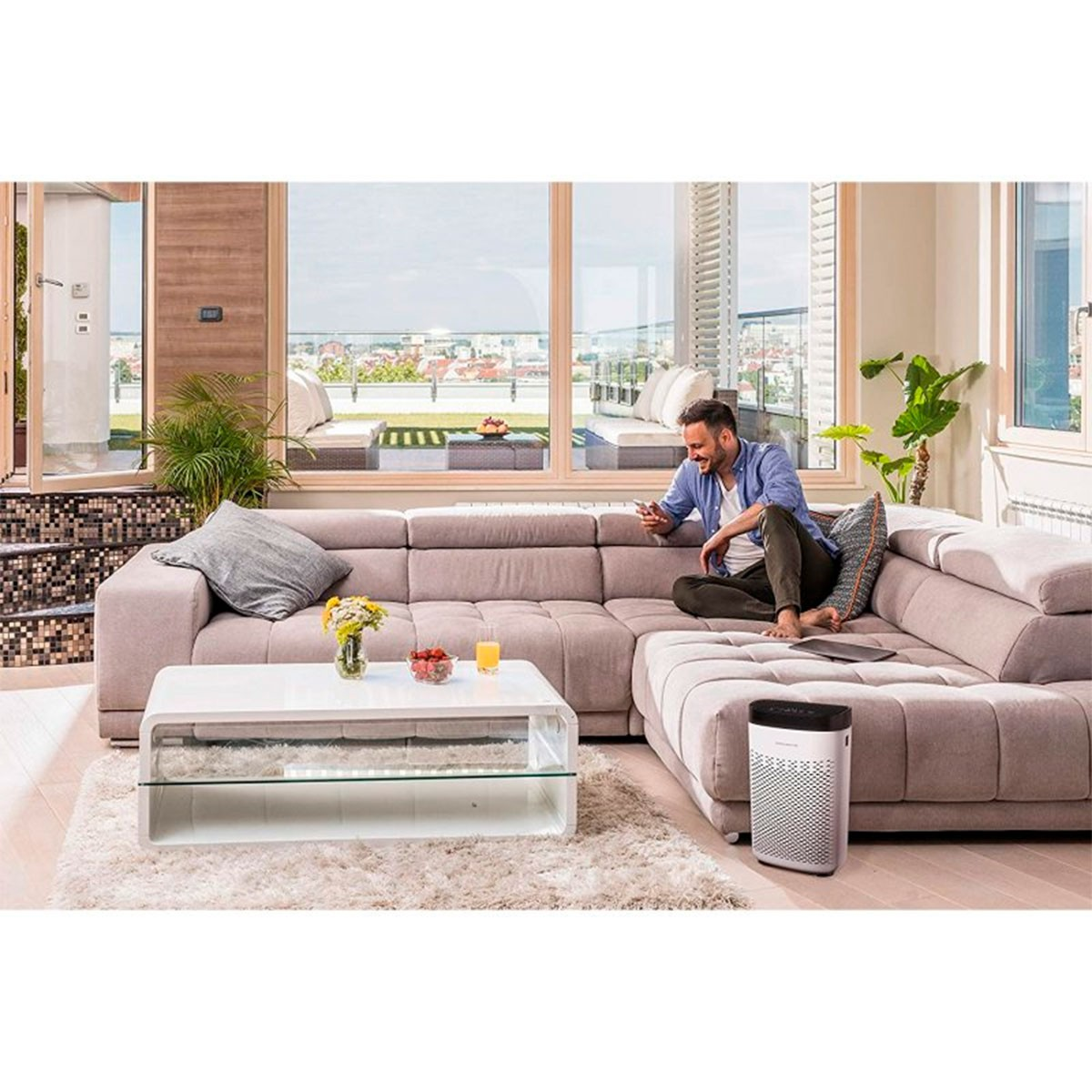 Ein Wohnzimmer mit einem Mann auf einem Sofa, der ein Telefon benutzt. Es gibt einen Couchtisch und einen Luftreiniger.