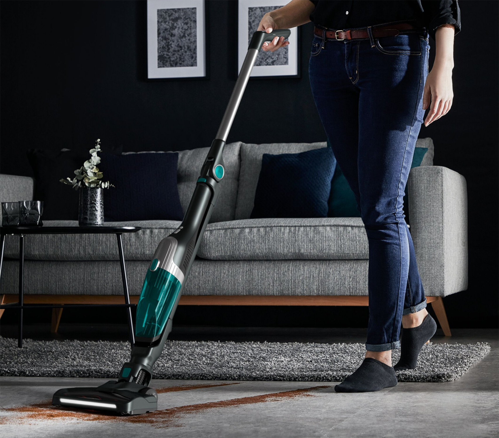Una persona che aspira un tappeto marrone con un aspirapolvere verde acqua e nero.