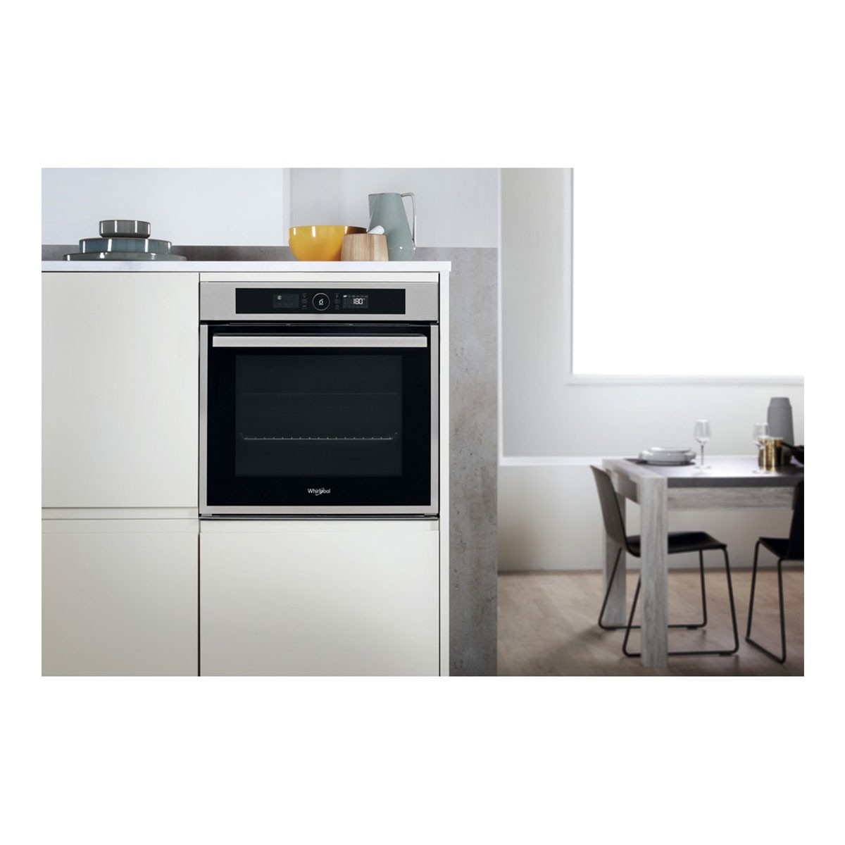 Horno empotrado con pantalla digital. Entorno de cocina con mesa y sillas al fondo.