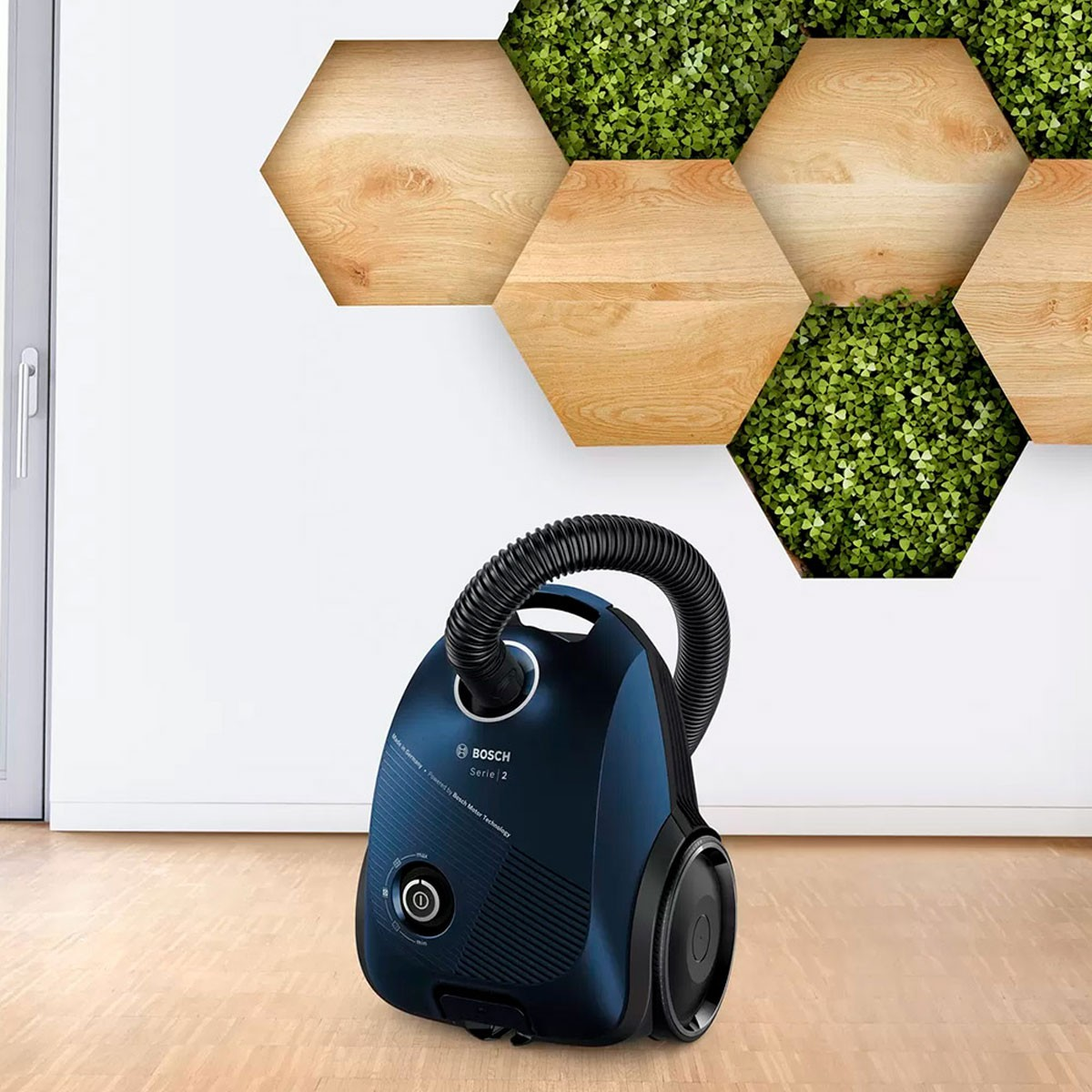 Niebieski odkurzacz na drewnianej podłodze, z sześciokątnym wzorem na ścianie.