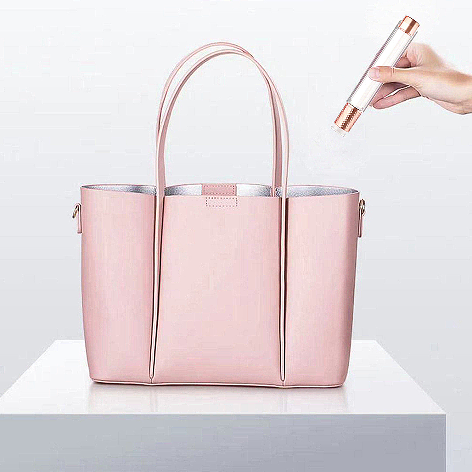 Borsa rosa su un tavolo bianco, una mano che tiene un dispositivo di bellezza sopra.