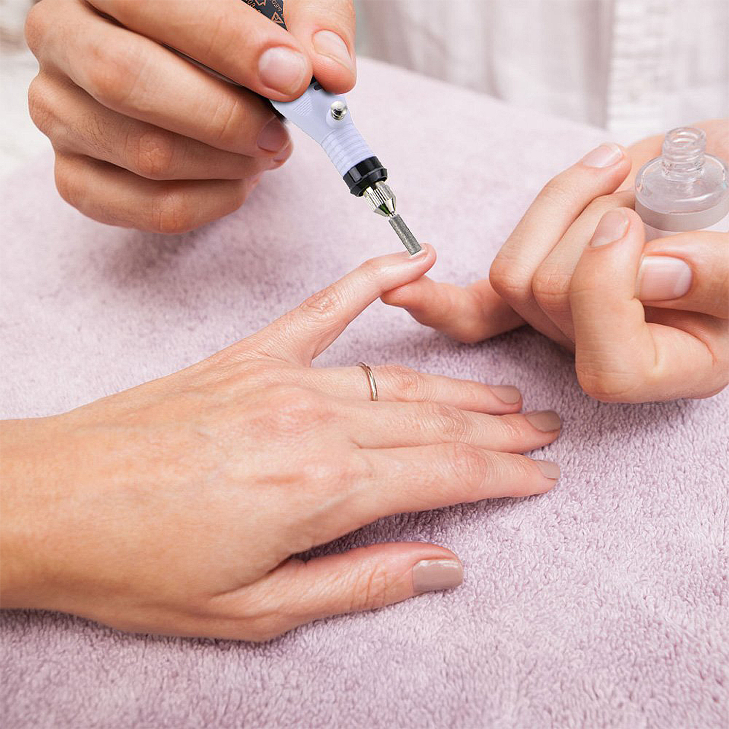 Hände, die eine Nagelbohrmaschine verwenden, um einen Nagel auf einem rosa Handtuch zu formen.