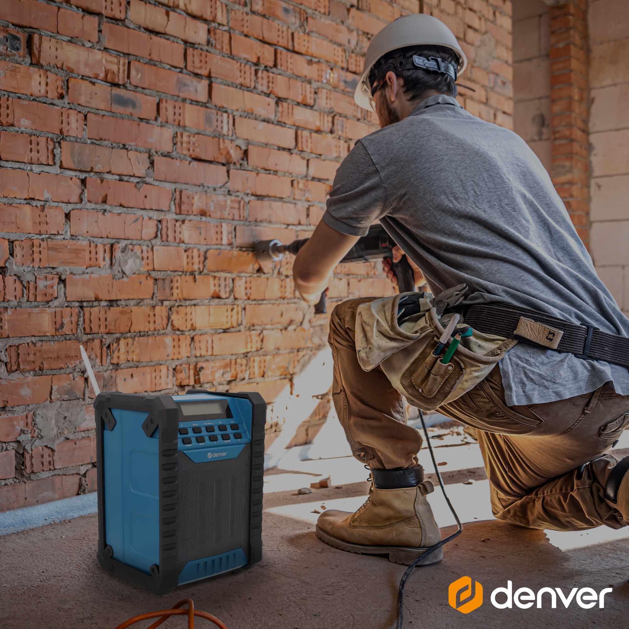 Mężczyzna wierci w ceglanej ścianie, z niebiesko-czarnym głośnikiem Denver na pierwszym planie.