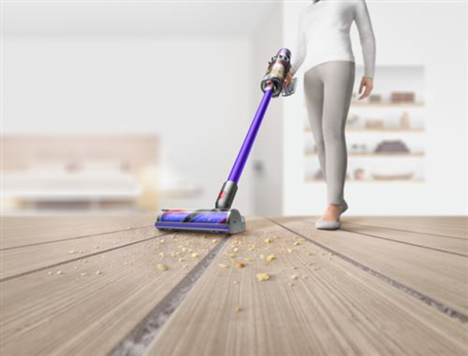 Osoba odkurza drewnianą podłogę, odkurzaczem Dyson. Widoczny kurz i brud.